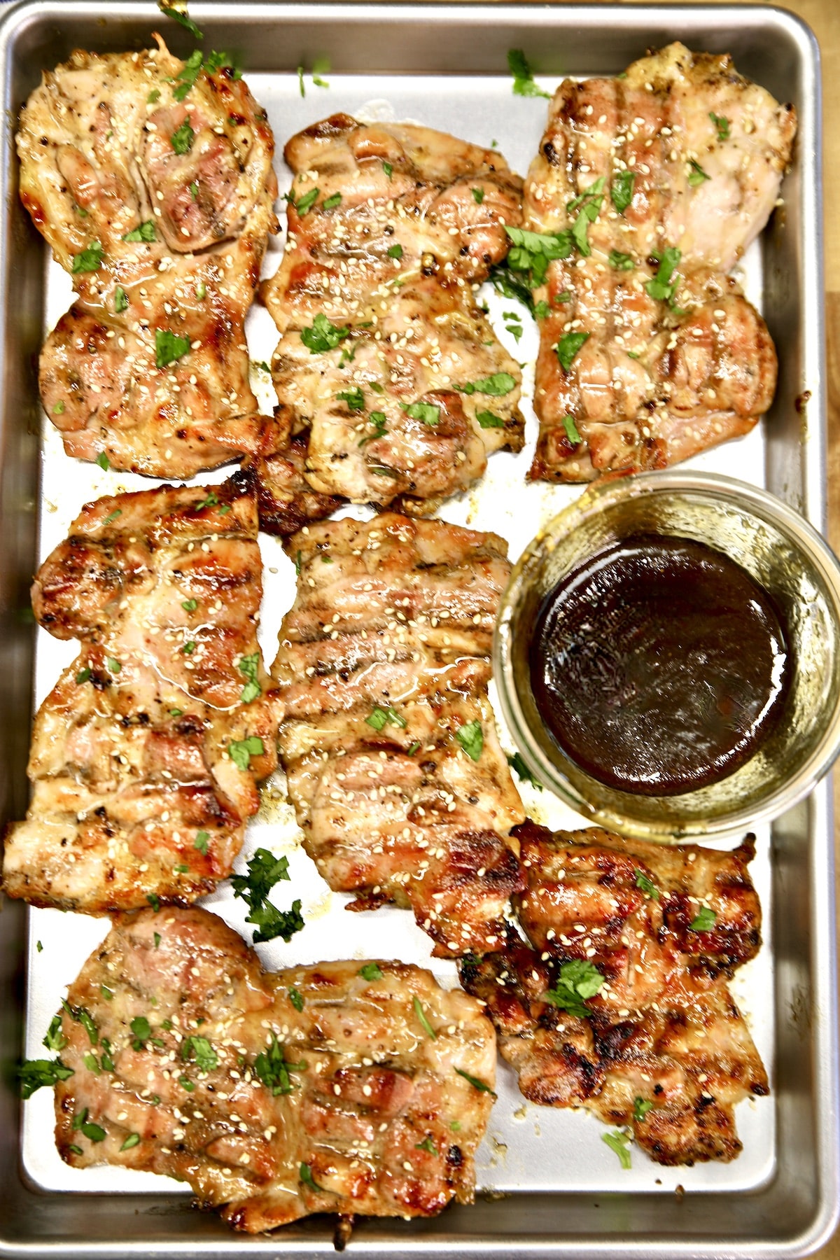 Sheet pan with grilled chicken thighs and Asian sauce in a bowl.