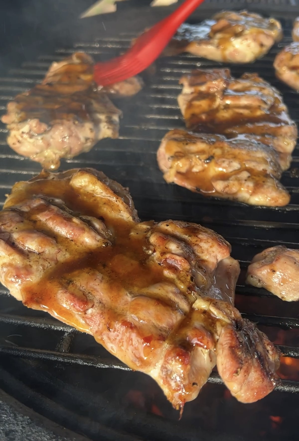 Brushing glaze over chicken thighs on a grill.