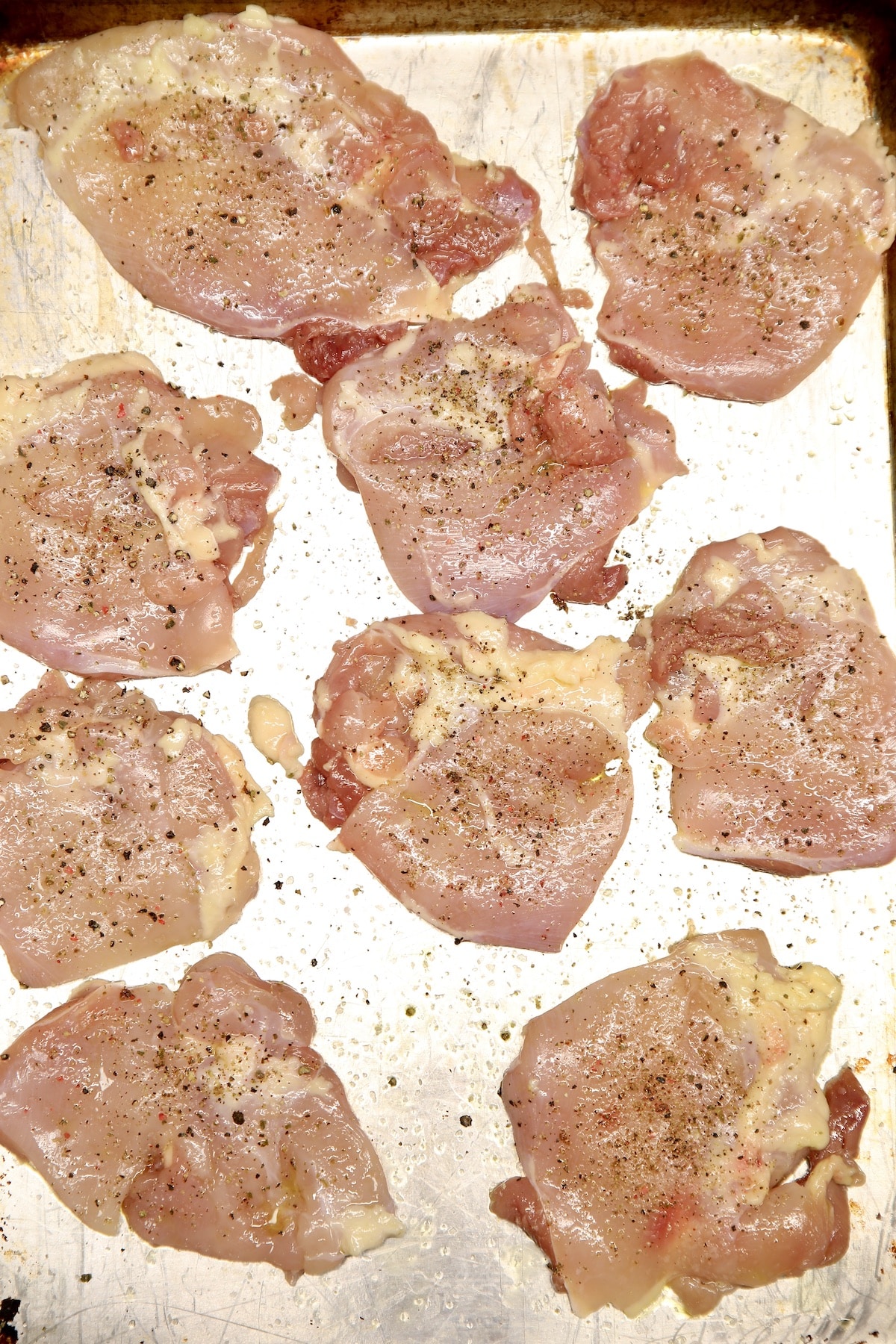Raw boneless skinless chicken thighs seasoned with salt and pepper on a baking sheet.