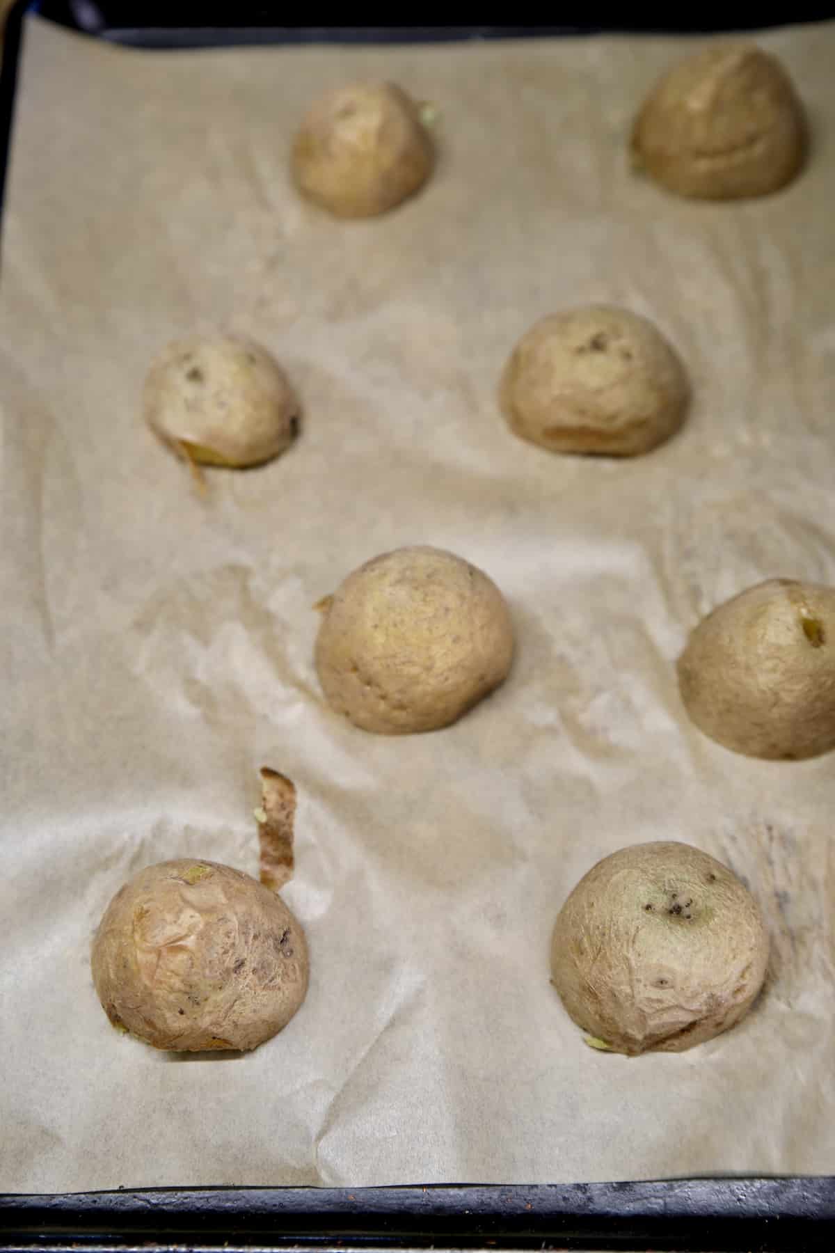Yukon gold potatoes cut in half on a lined baking sheet.