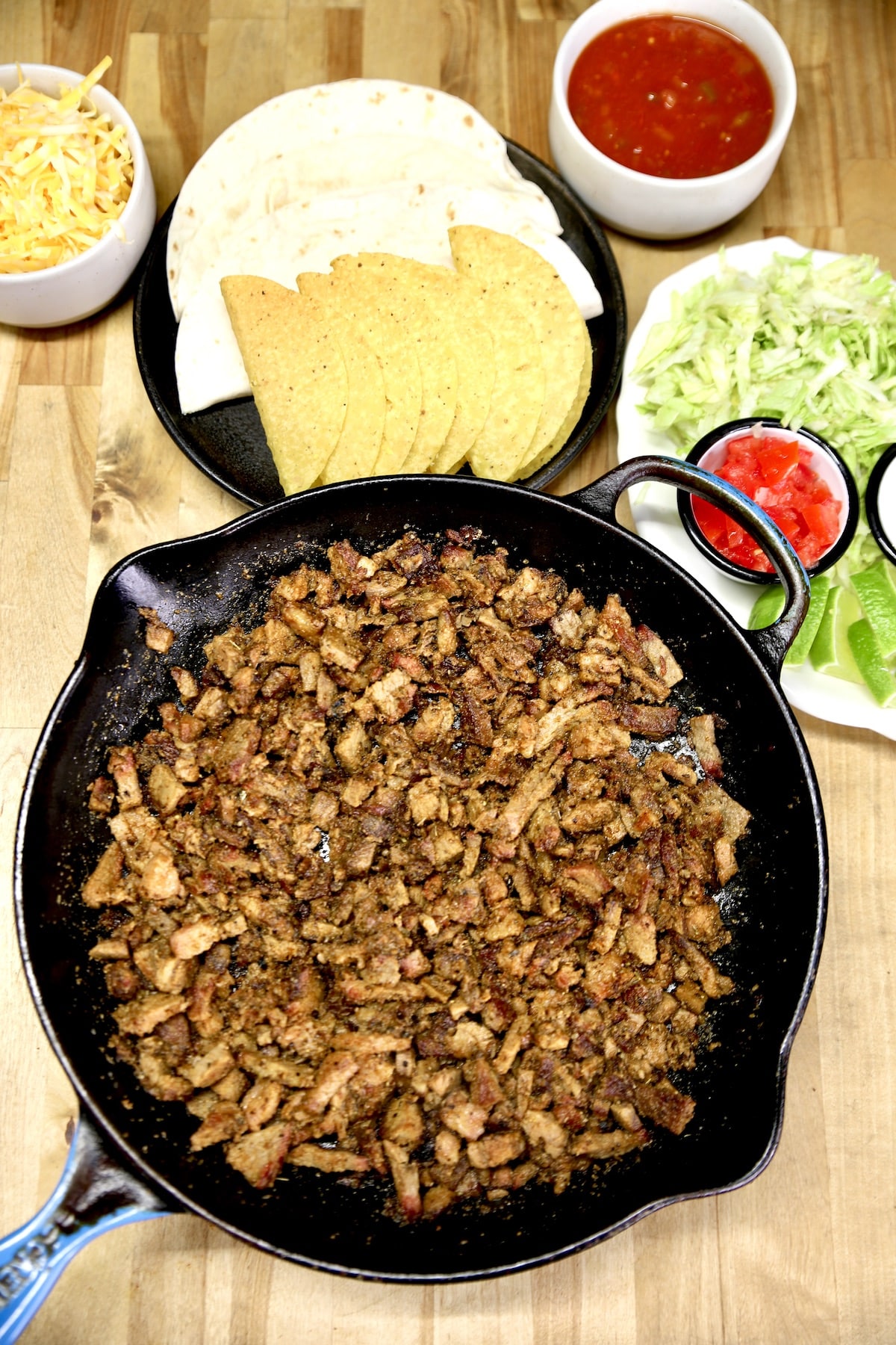 Skillet of chopped brisket, taco shells, toppings.