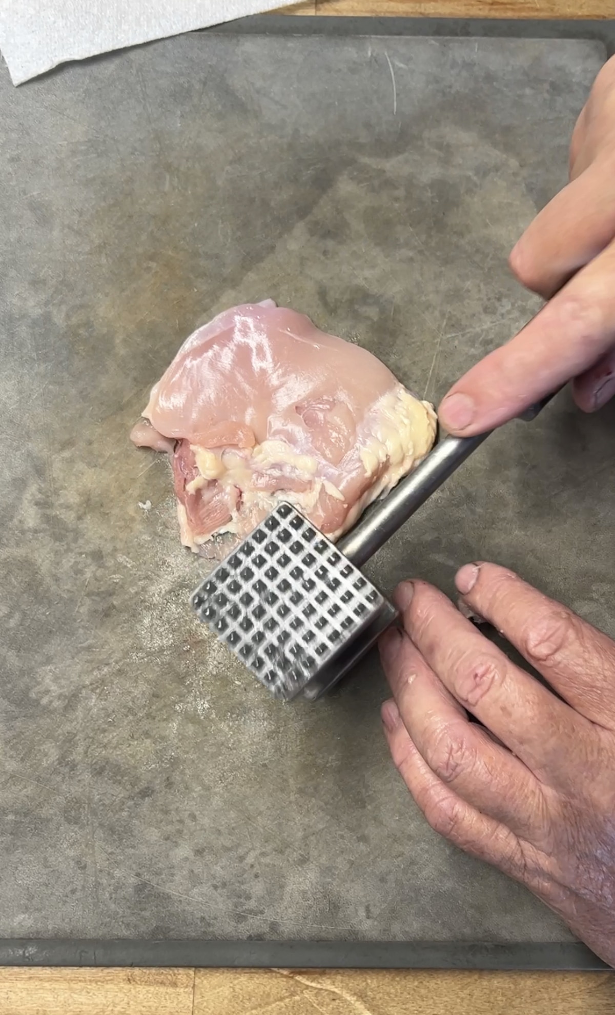 Pounding chicken thighs flat with meat mallet.