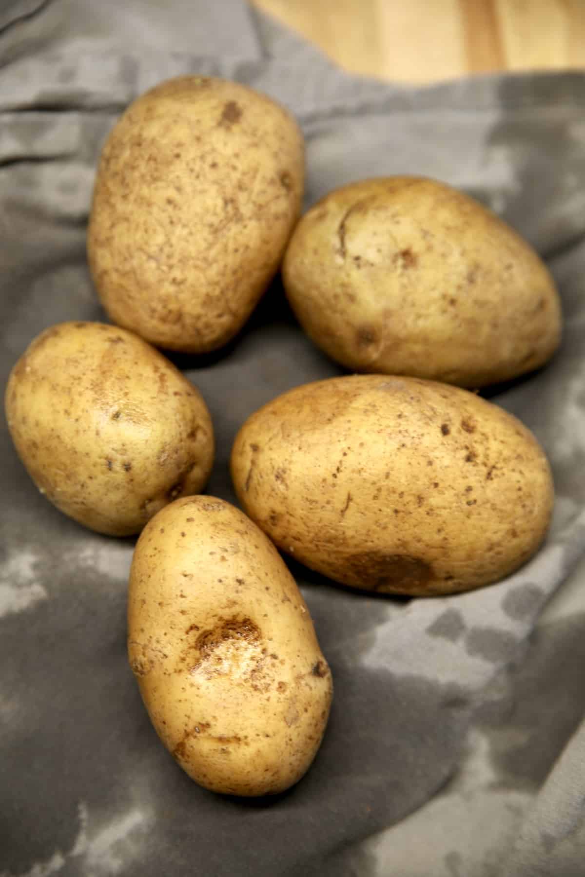 4 Yukon gold potatoes, washed and drying on a gray towel.