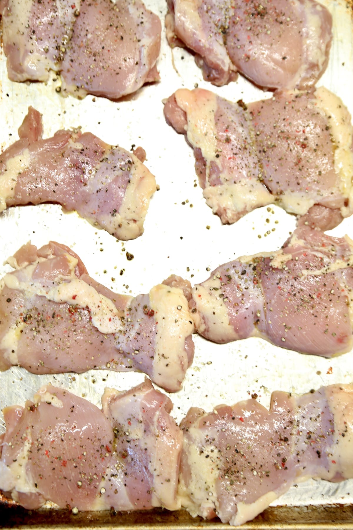 Sheet pan with raw chicken thighs, seasoned with salt and pepper.