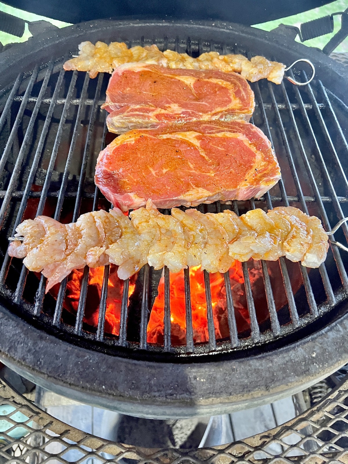 2 ribeye steaks with 2 skewers of shrimp on a grill.