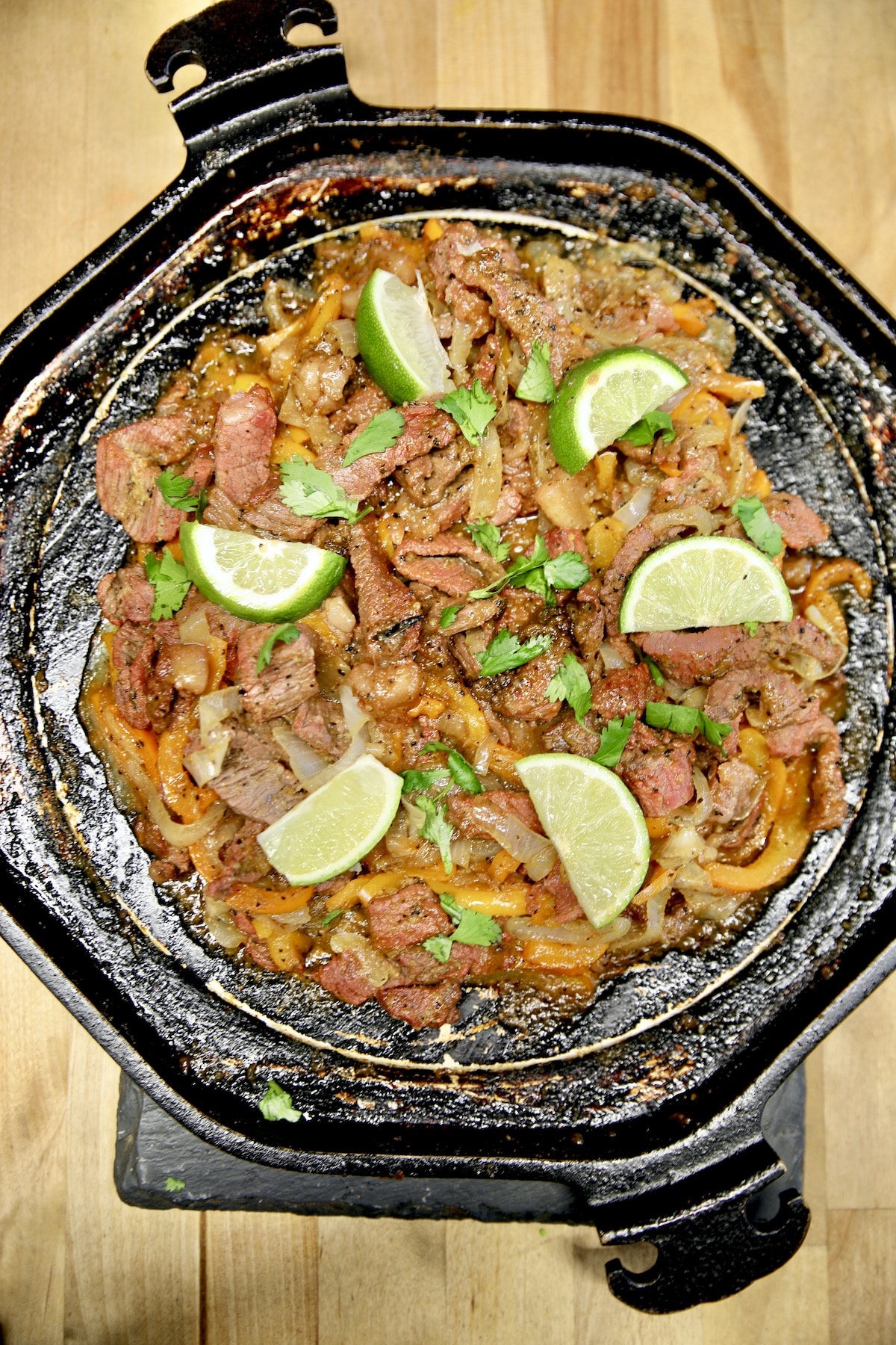 Griddle pan with steak fajitas, garnished with lime slices.