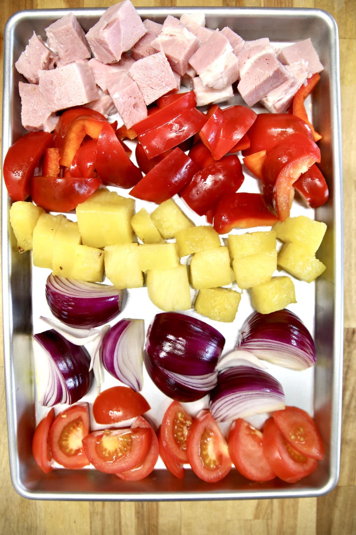 Tray with ham chunks, , red bell peppers, pineapple, red onions, tomatoes.