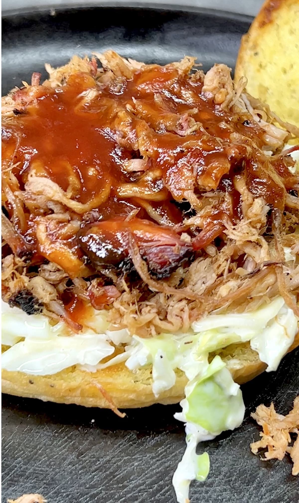 Closeup of pulled pork sandwich with top bun off. Drizzled with bbq sauce.