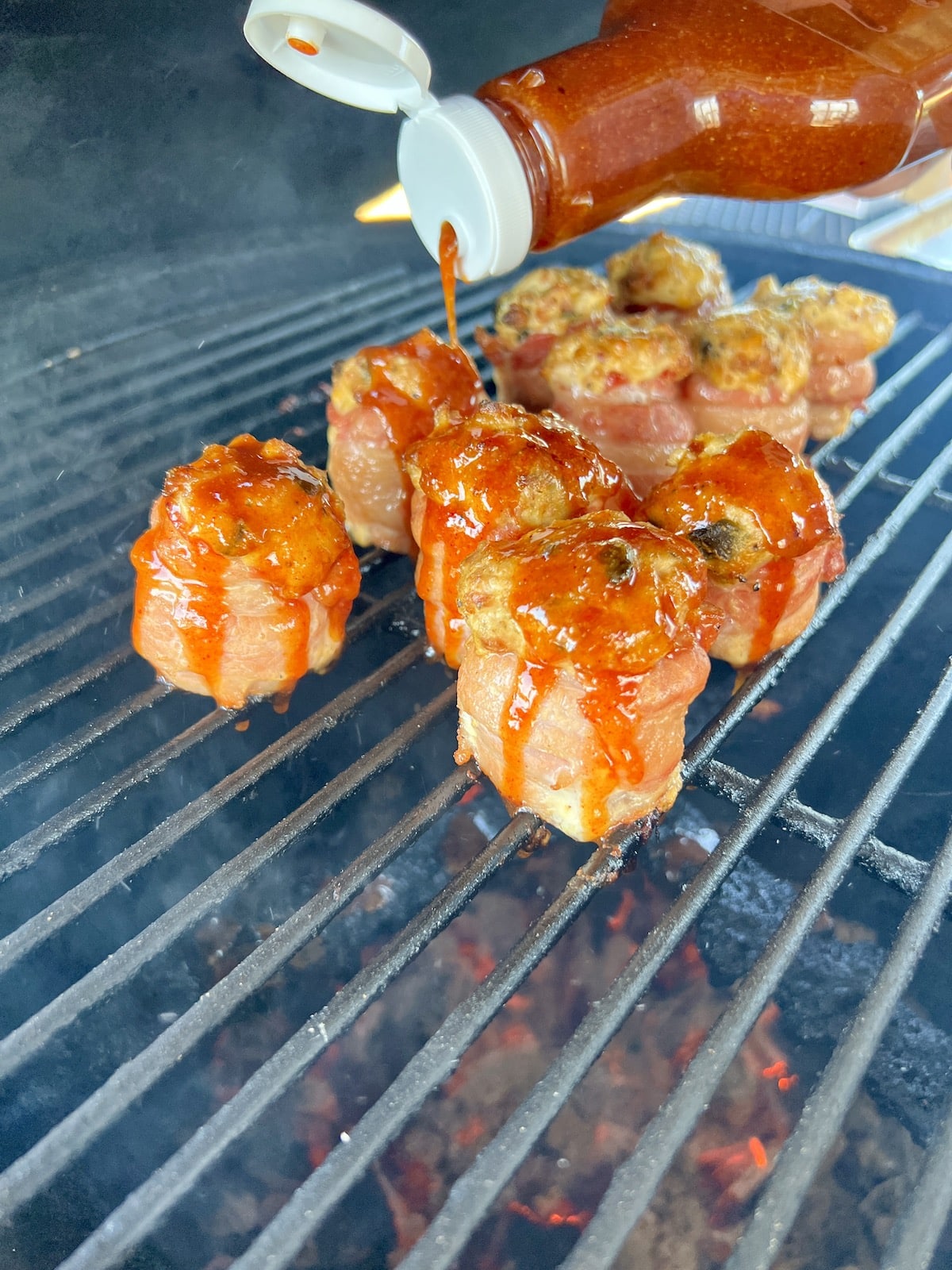 Drizzling peach bbq sauce over pig shots on a grill.