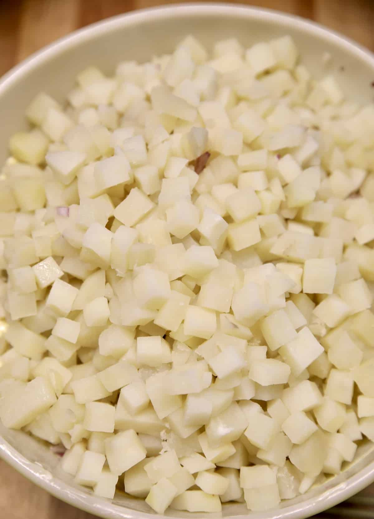 Adding diced potatoes to a bowl with dressing.