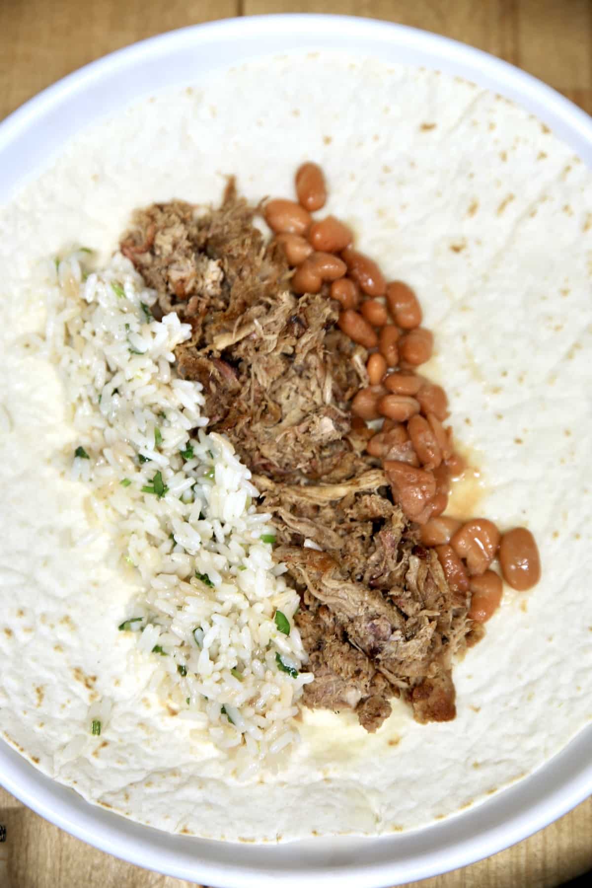 Making a burrito with rice, pulled pork, pinto beans.
