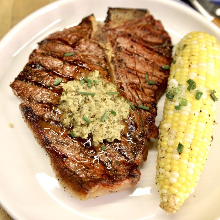 T-Bone Steak topped with garlic and herb butter on a plate with corn on the cob.