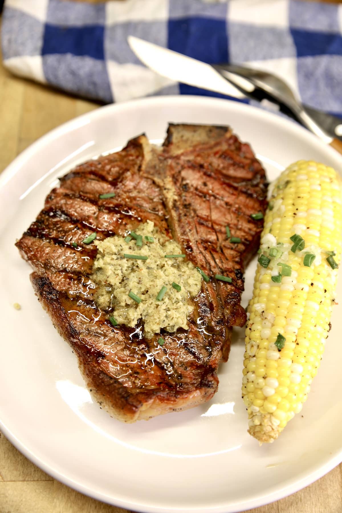Plate of grilled T-Bone steak topped with butter, corn on the cob.