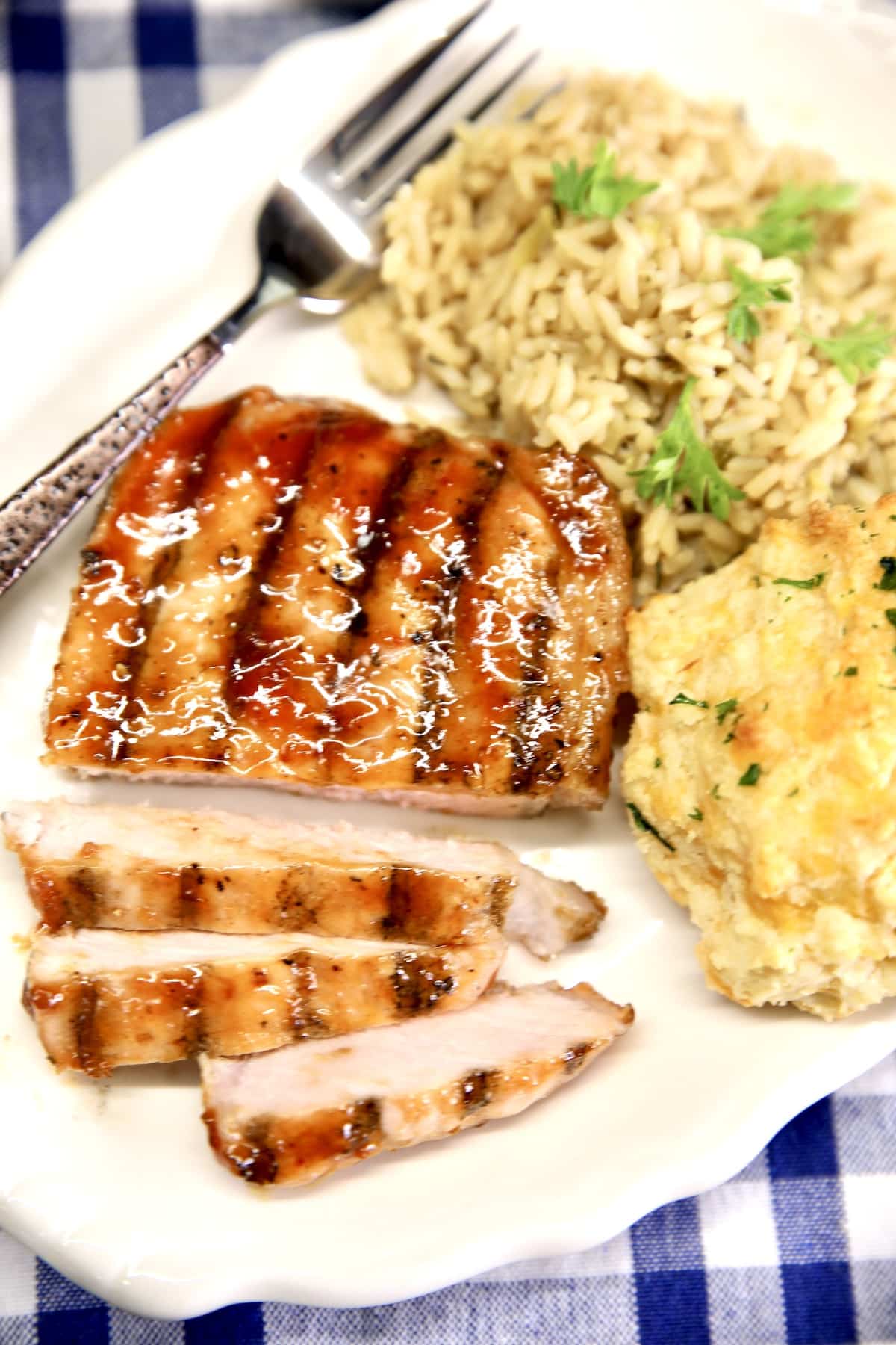 Grilled pork chop on a plate with rice and a biscuit.