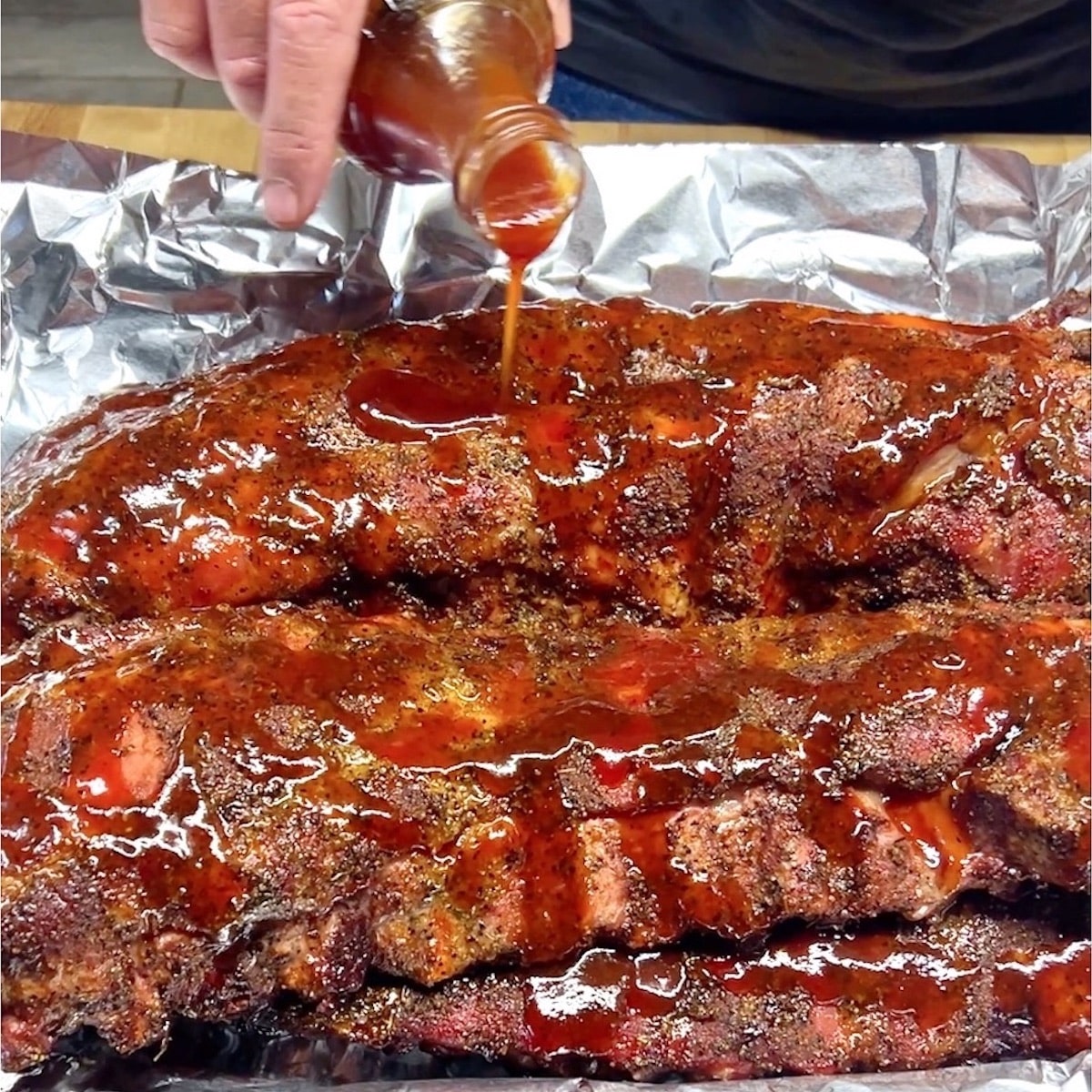 Pouring BBQ Sauce over baby back ribs.