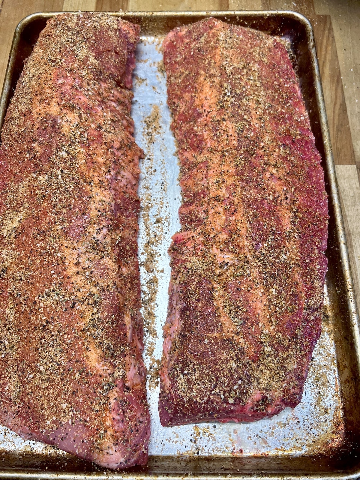 Dry rubbed baby back ribs on a sheet pan.