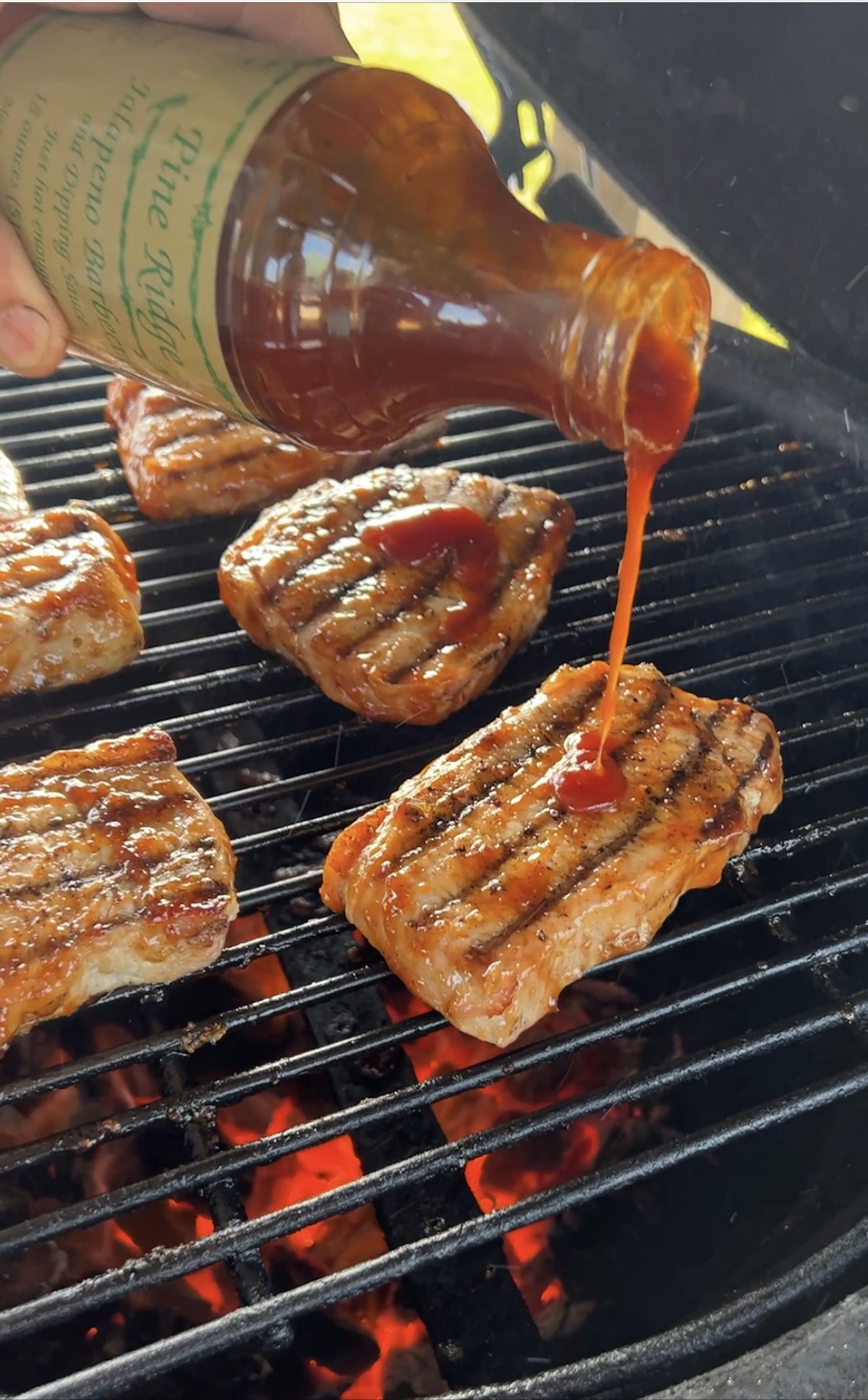 Pouring bbq sauce onto pork chops on a grill.