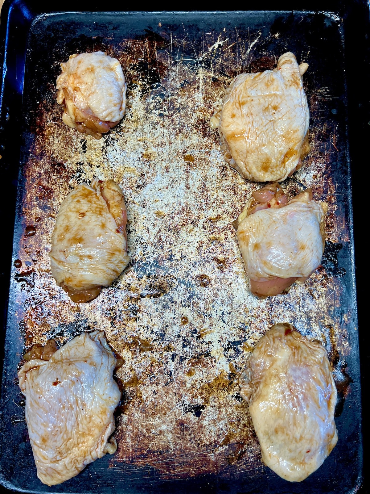 Marinated chicken thighs on a sheet pan.