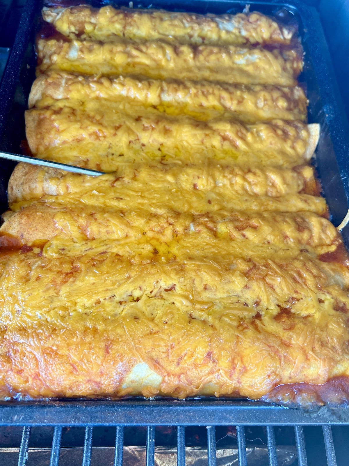 Pan of enchiladas with cheese on a grill.