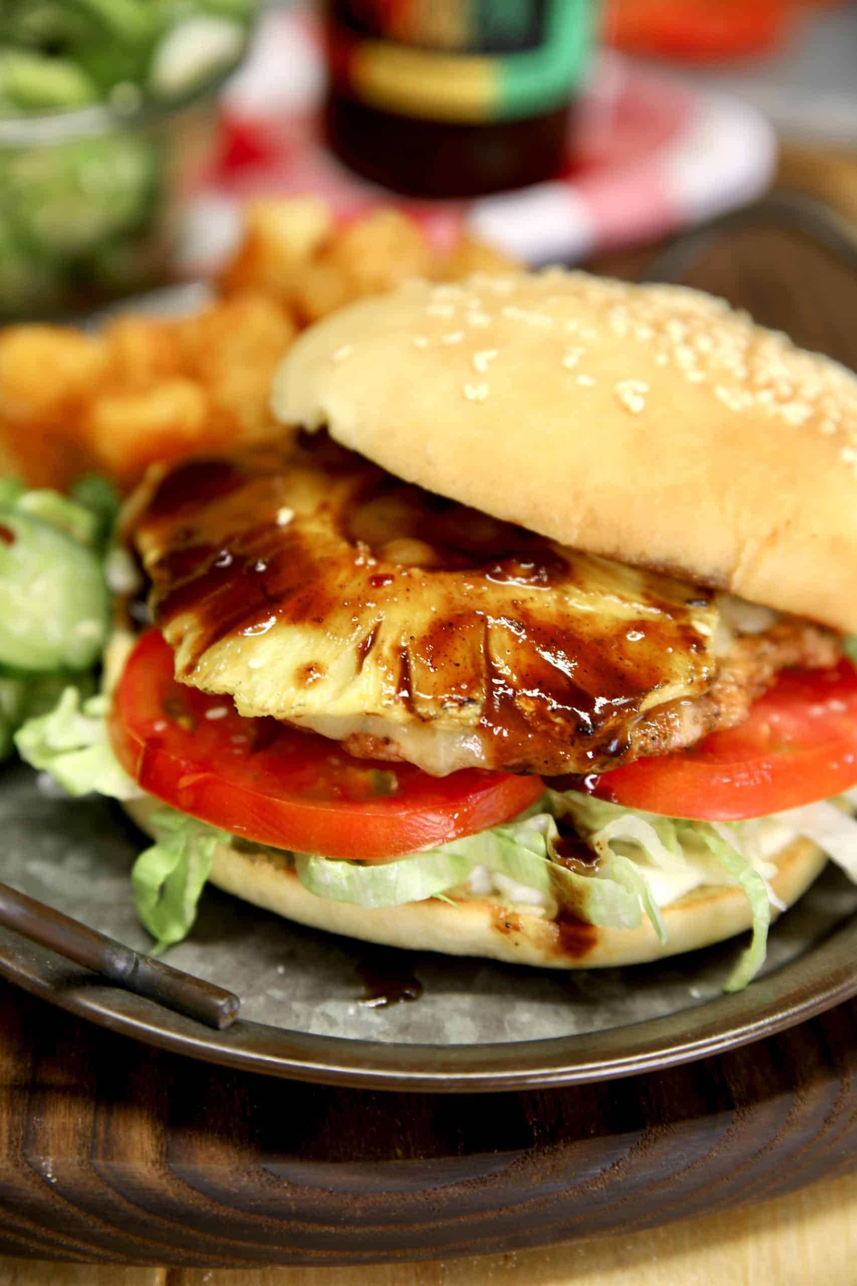 Closeup of jerk pork burger with jerk sauce, tomato, lettuce and grilled pineapple.