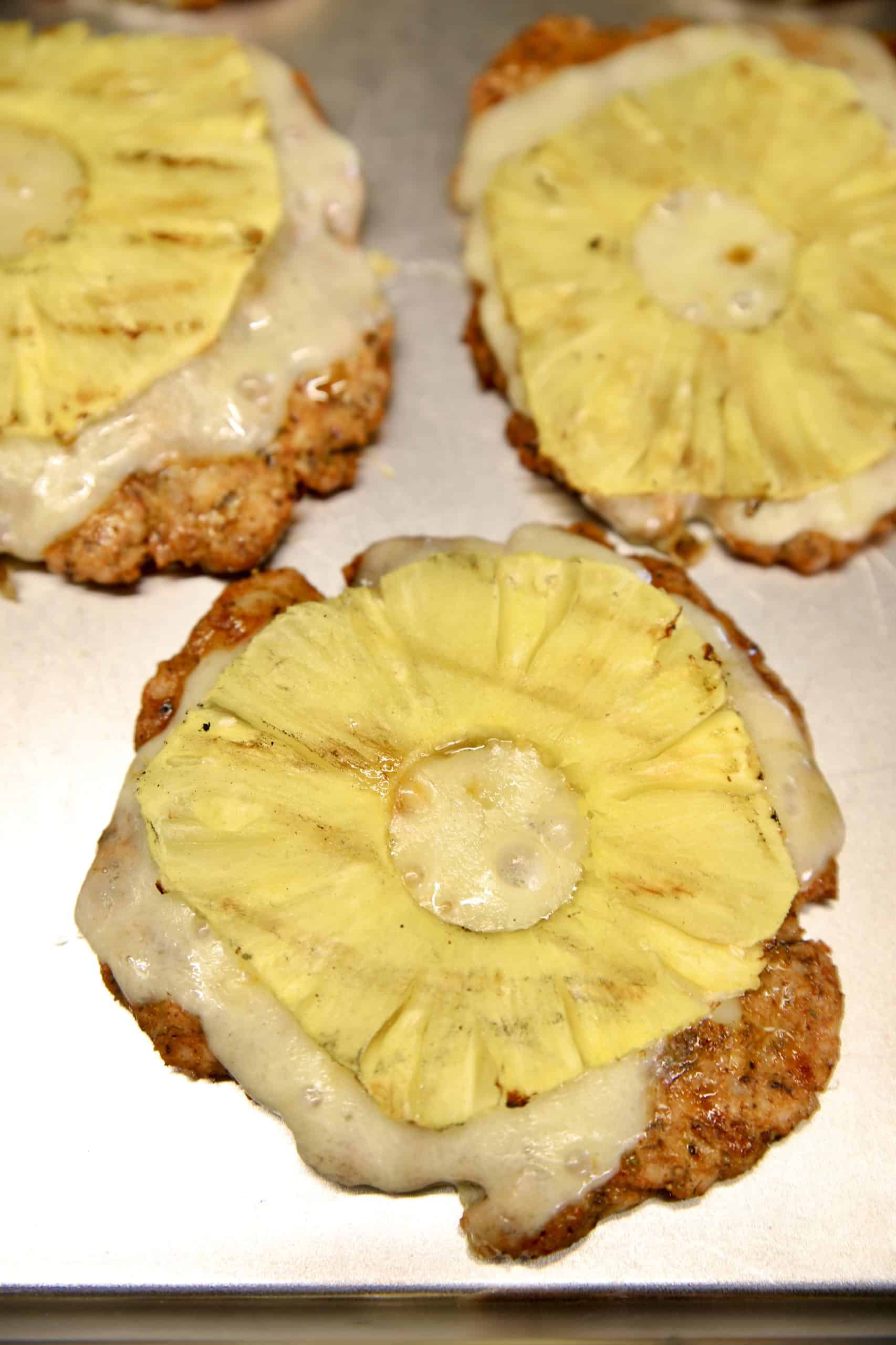 Grilled pork burgers with cheese and pineapple rings.
