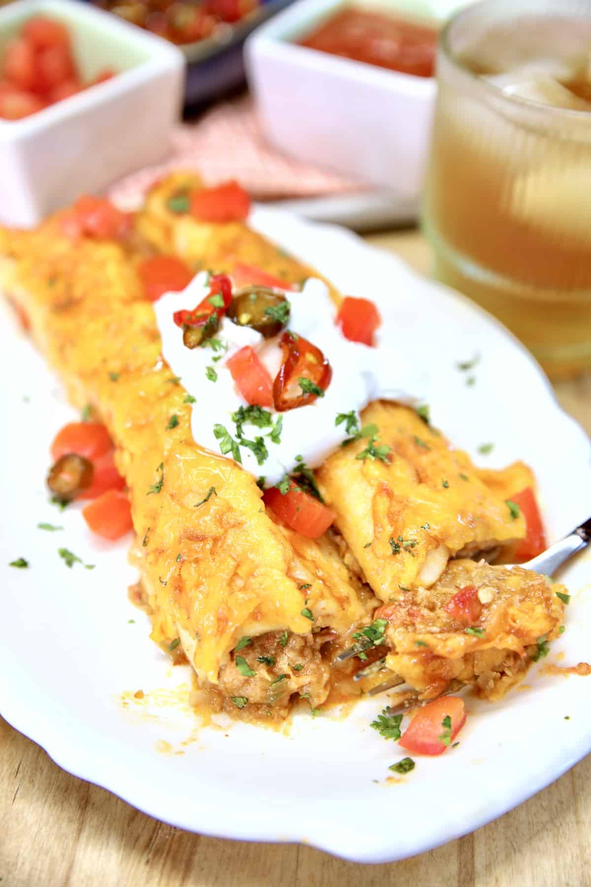 Plate with 2 pork enchiladas, topped with sour cream and tomatoes.