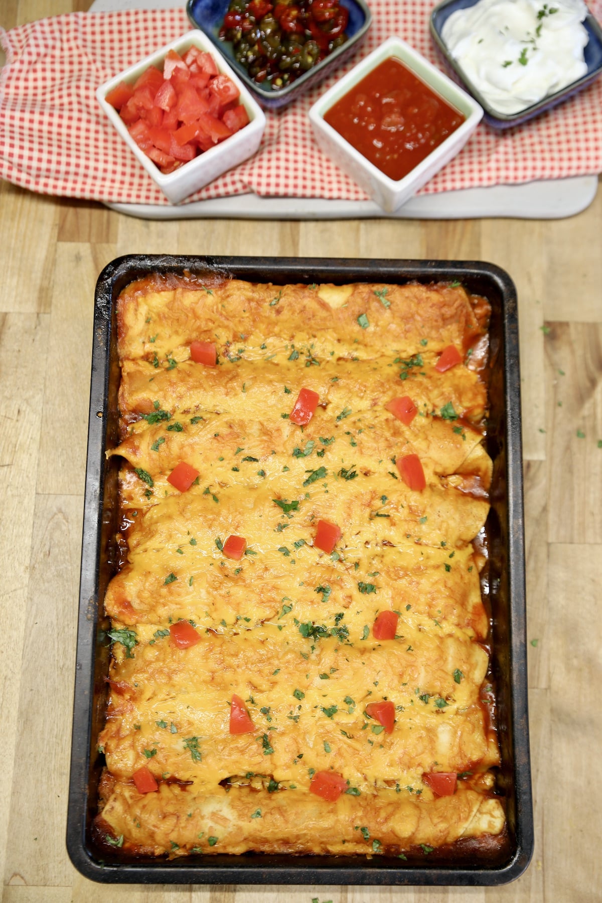 Pan of enchiladas with bowls of condiments.