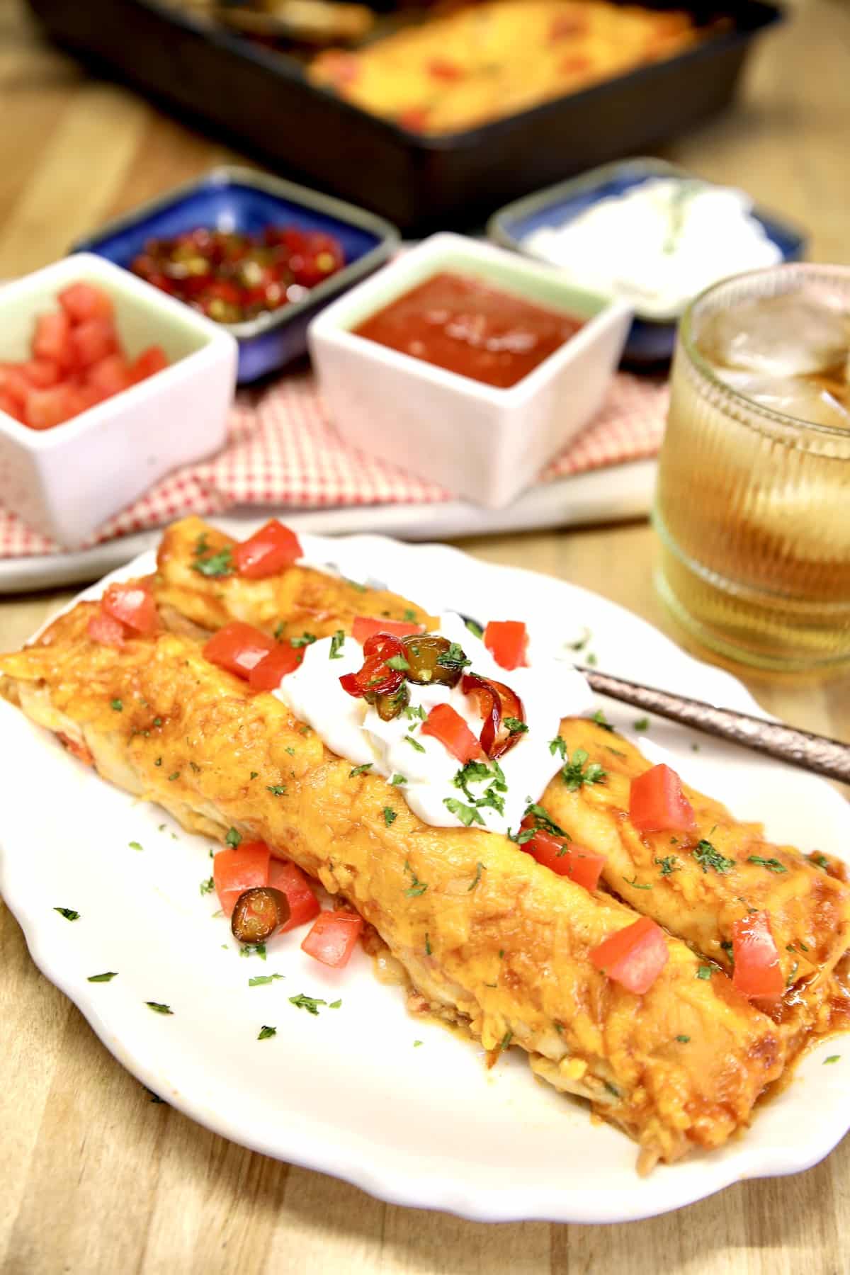 Plate with 2 enchiladas, sour cream and tomatoes.