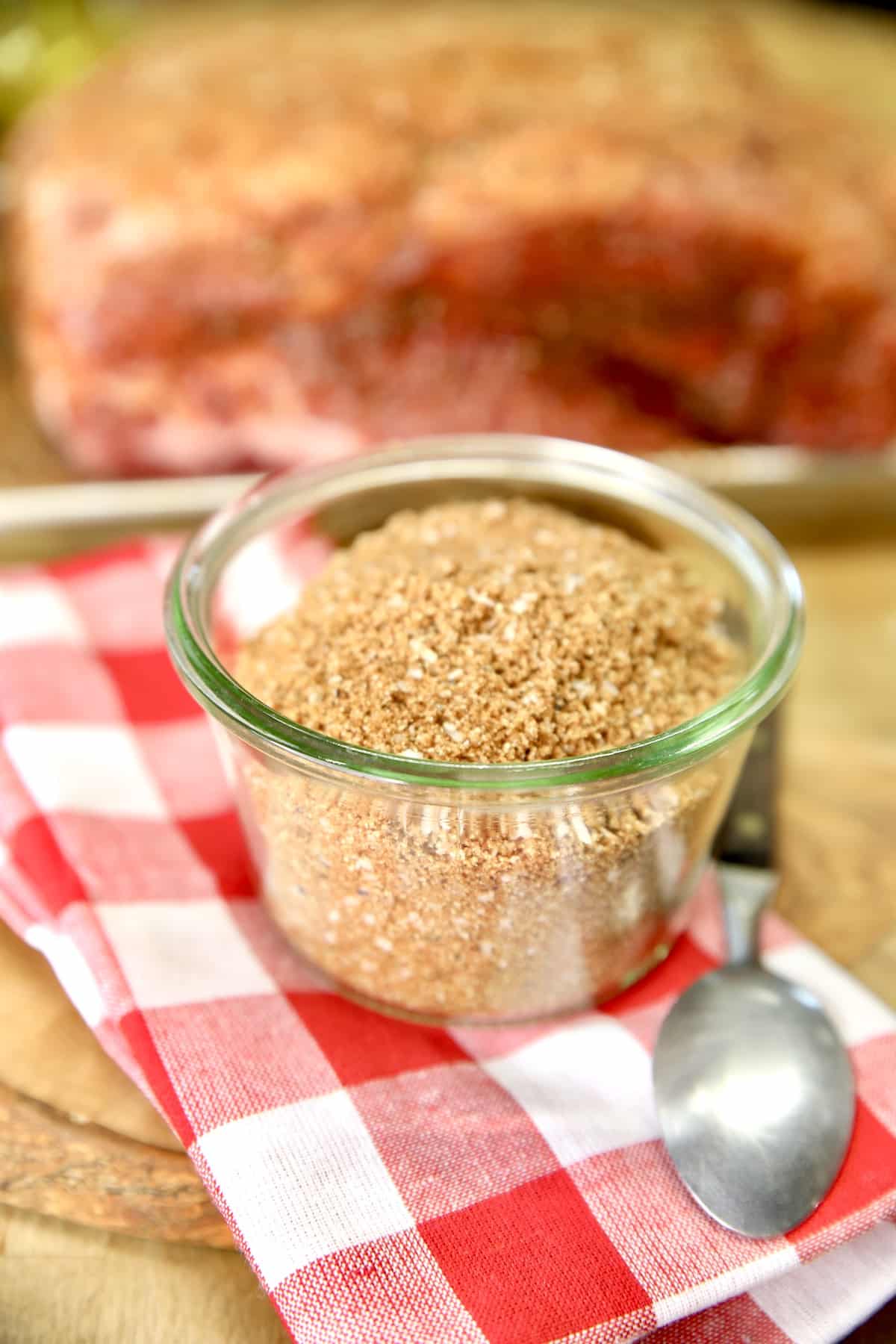 Jar of dry rub in front of a seasoned pork butt.