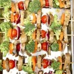 Sheet pan with uncooked vegetable kabobs.