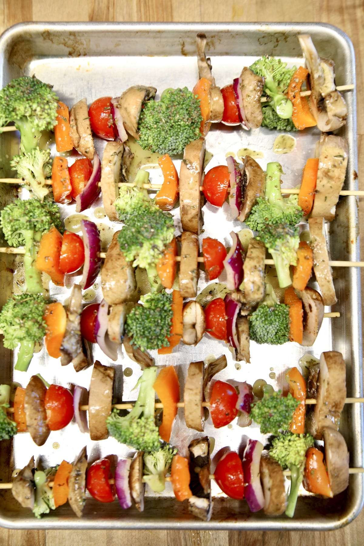 Sheet pan with uncooked vegetable kabobs.