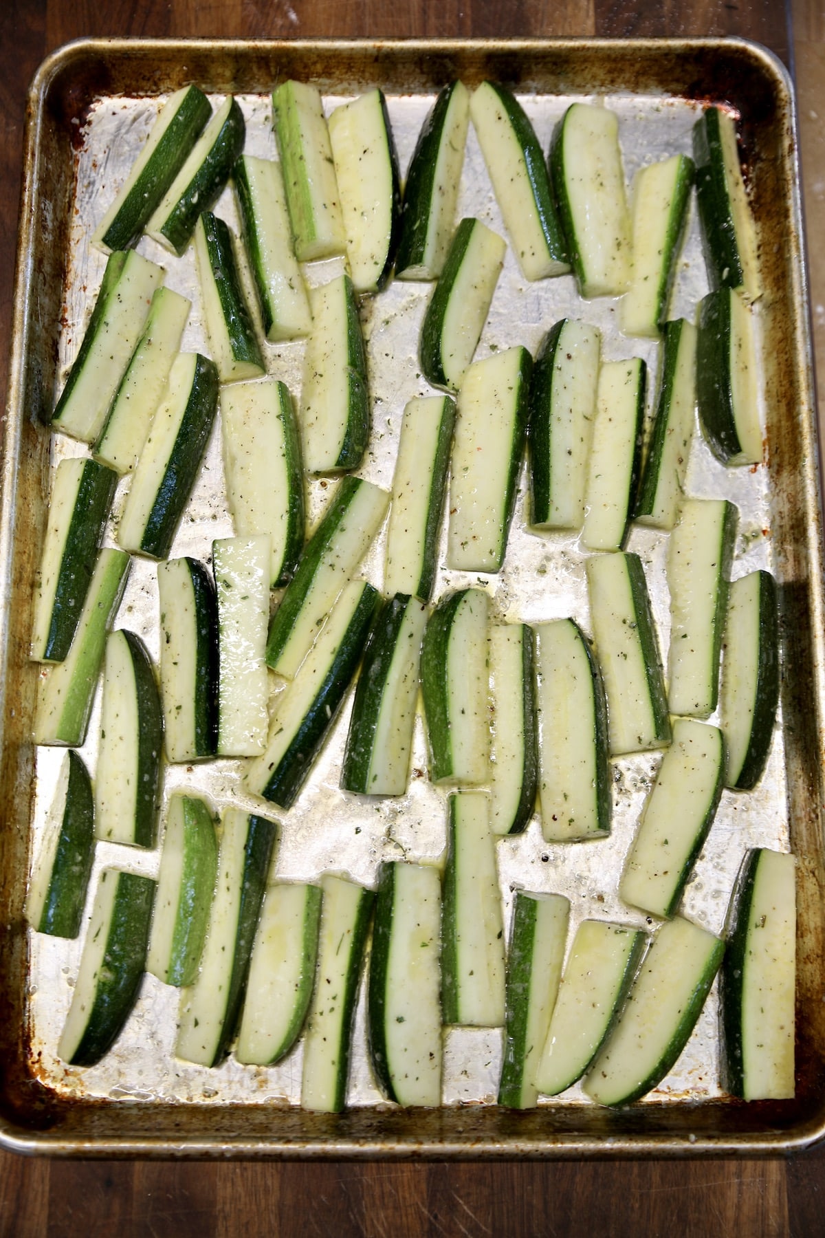 Zucchini spears spread onto a rimmed baking sheet.