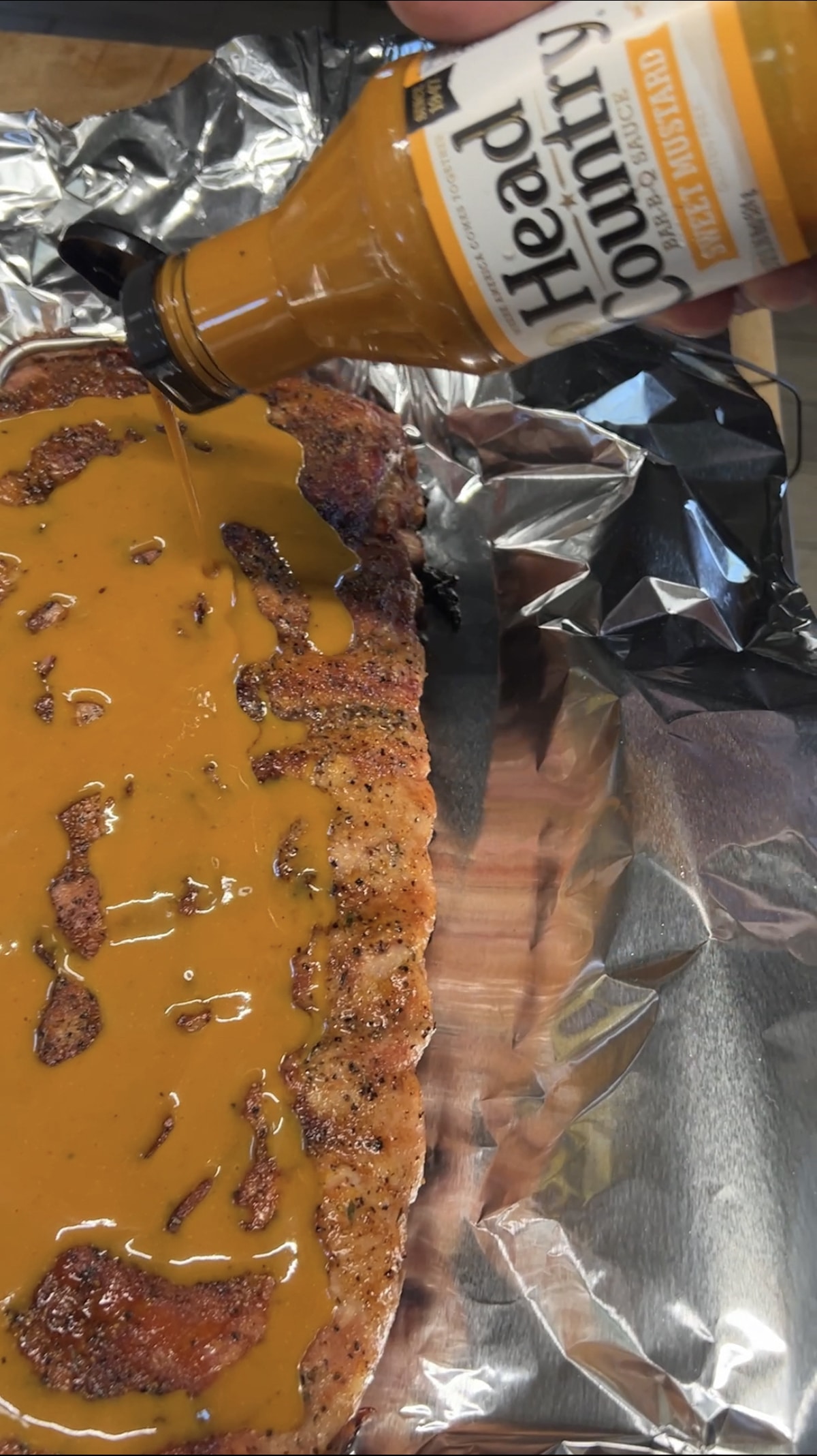 Ribs on foil, pouring sweet mustard over the top.