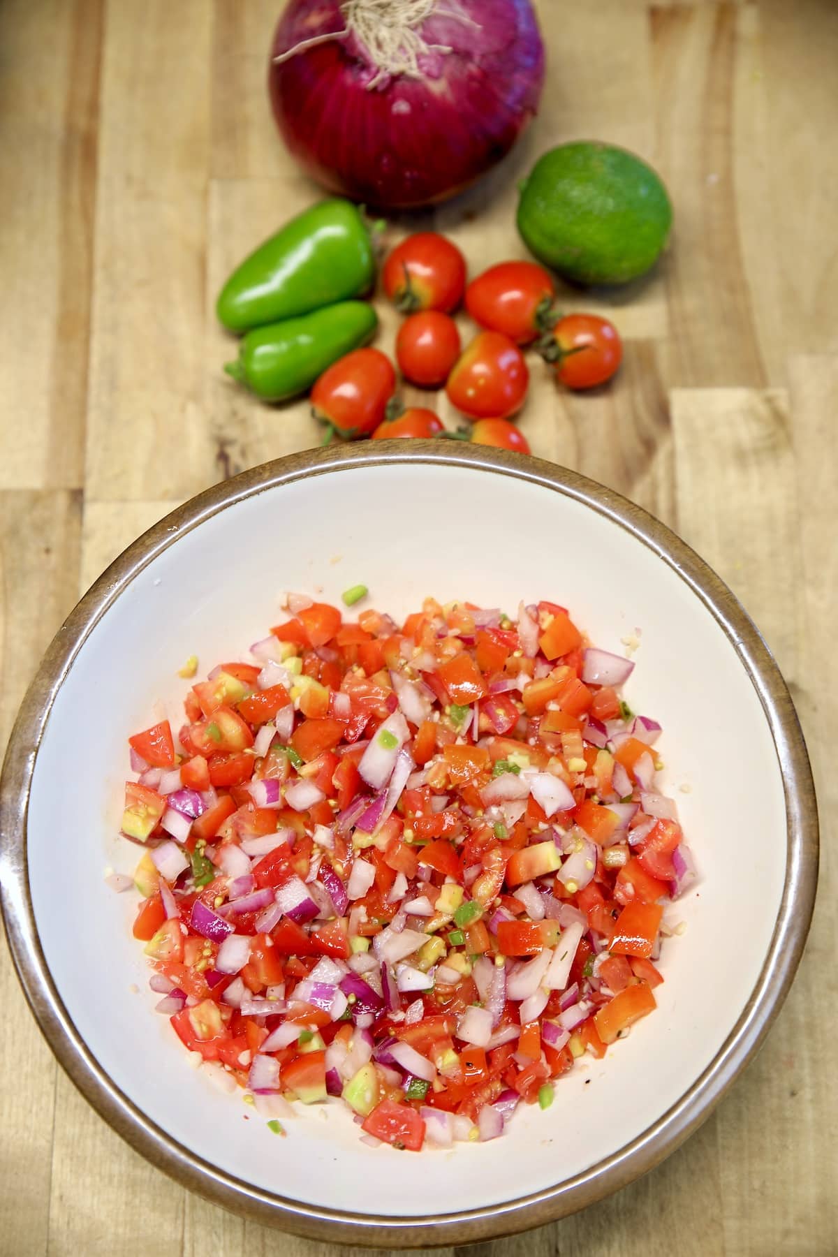 Bowl of salsa fresca with vegetables by the bowl.