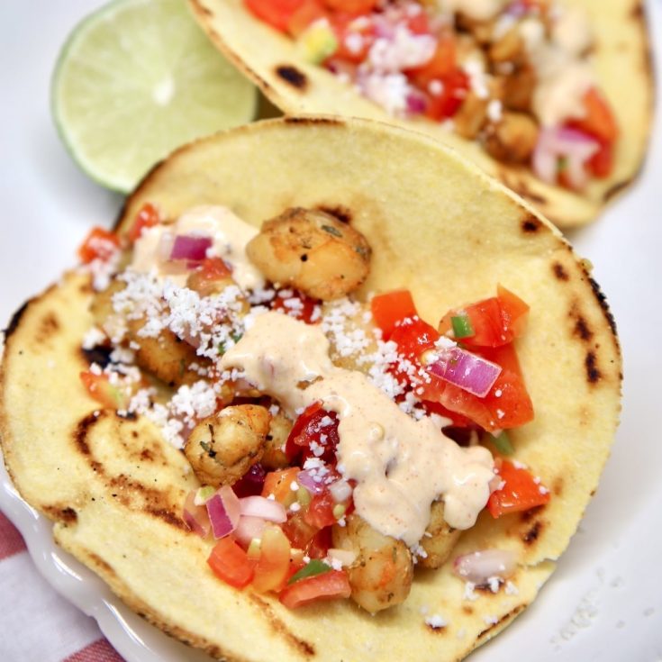 Seafood tacos on a plate with taco sauce.