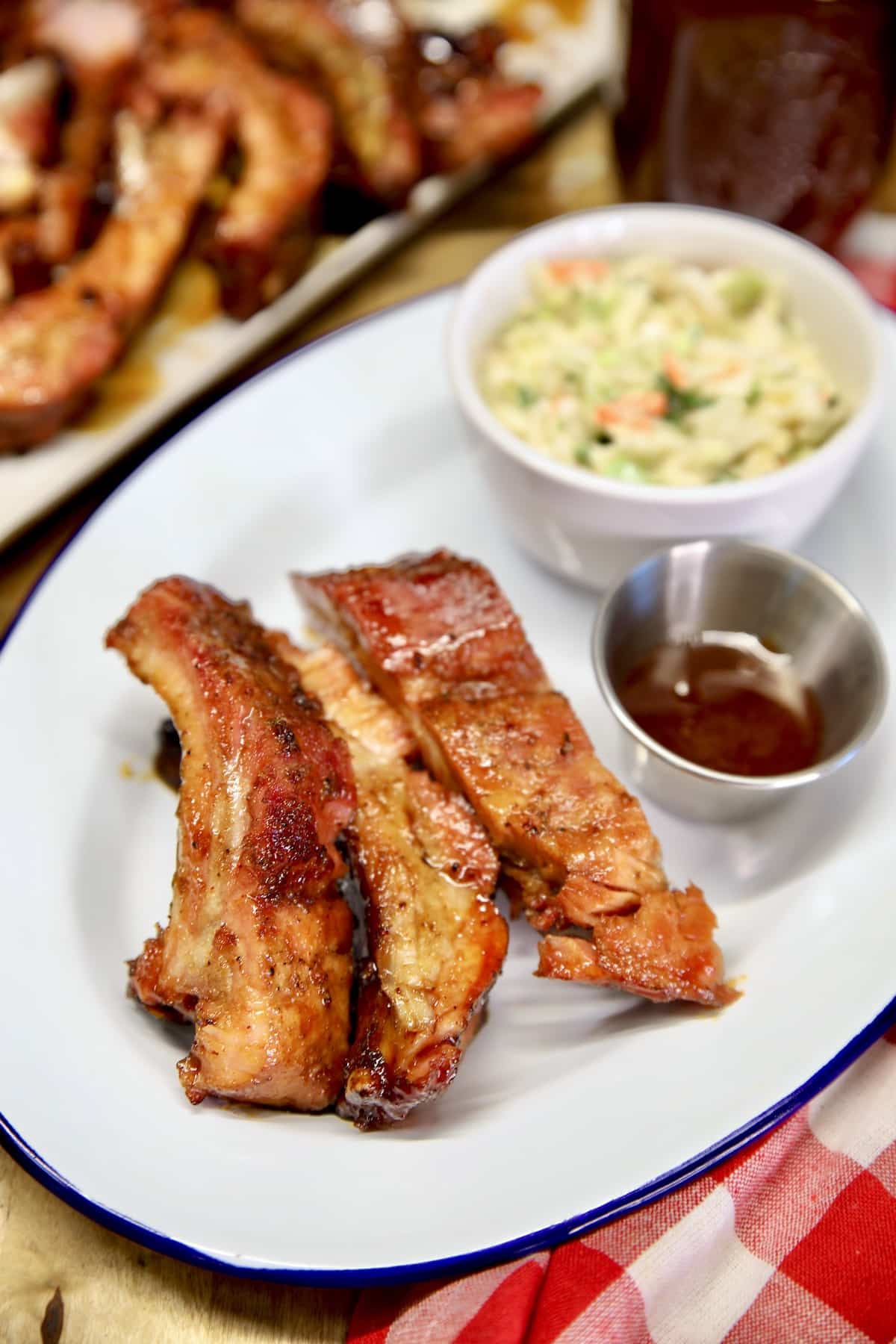 Honey garlic baby back ribs on a platter with sauce and slaw.