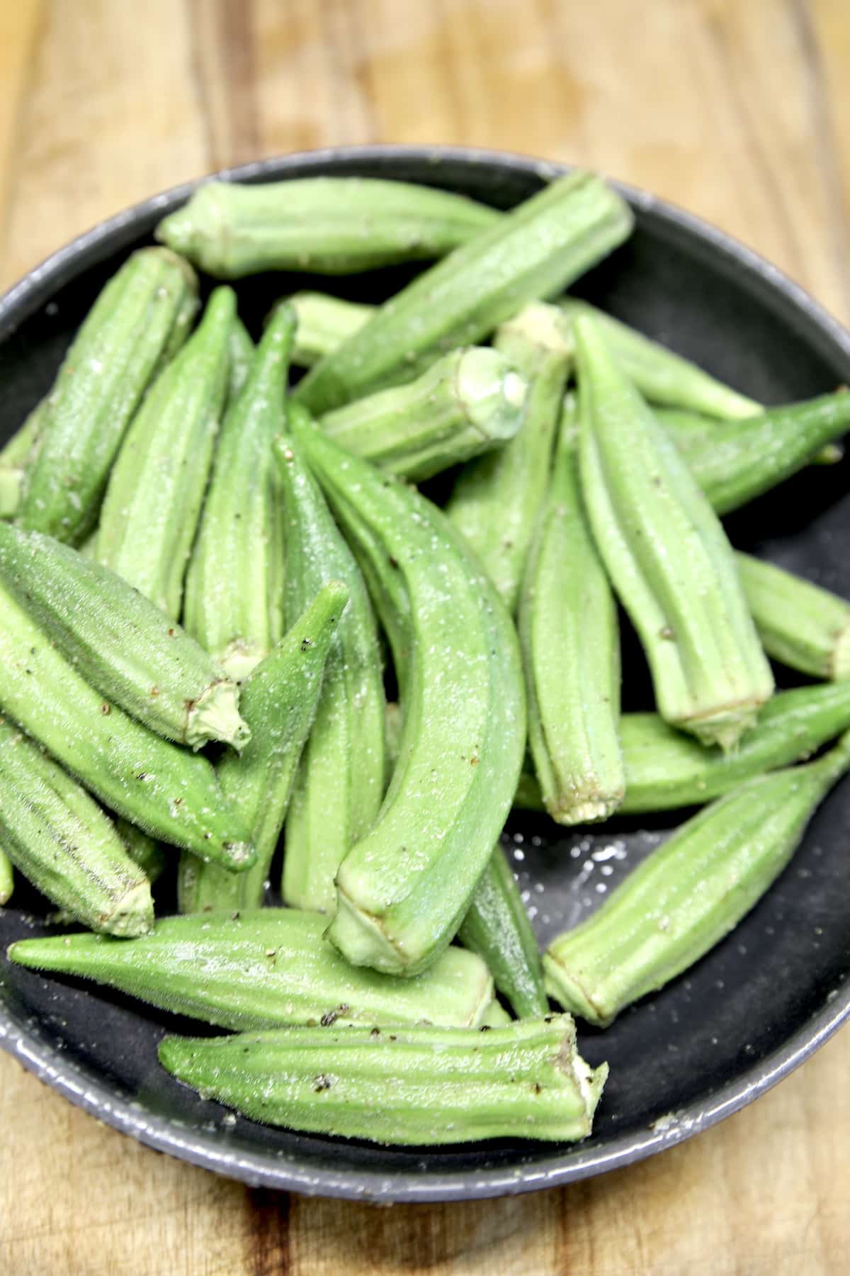 Fresh okra in a bowl with olive oil and spices.