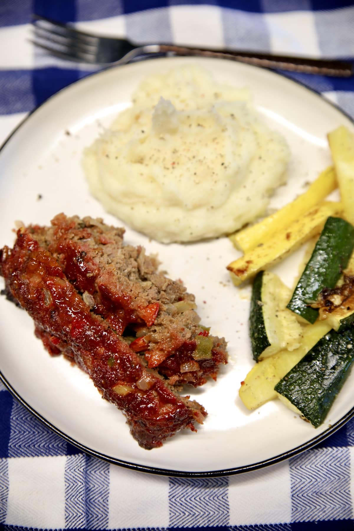 2 slices meatloaf on a plate with mashed potatoes and zucchini.