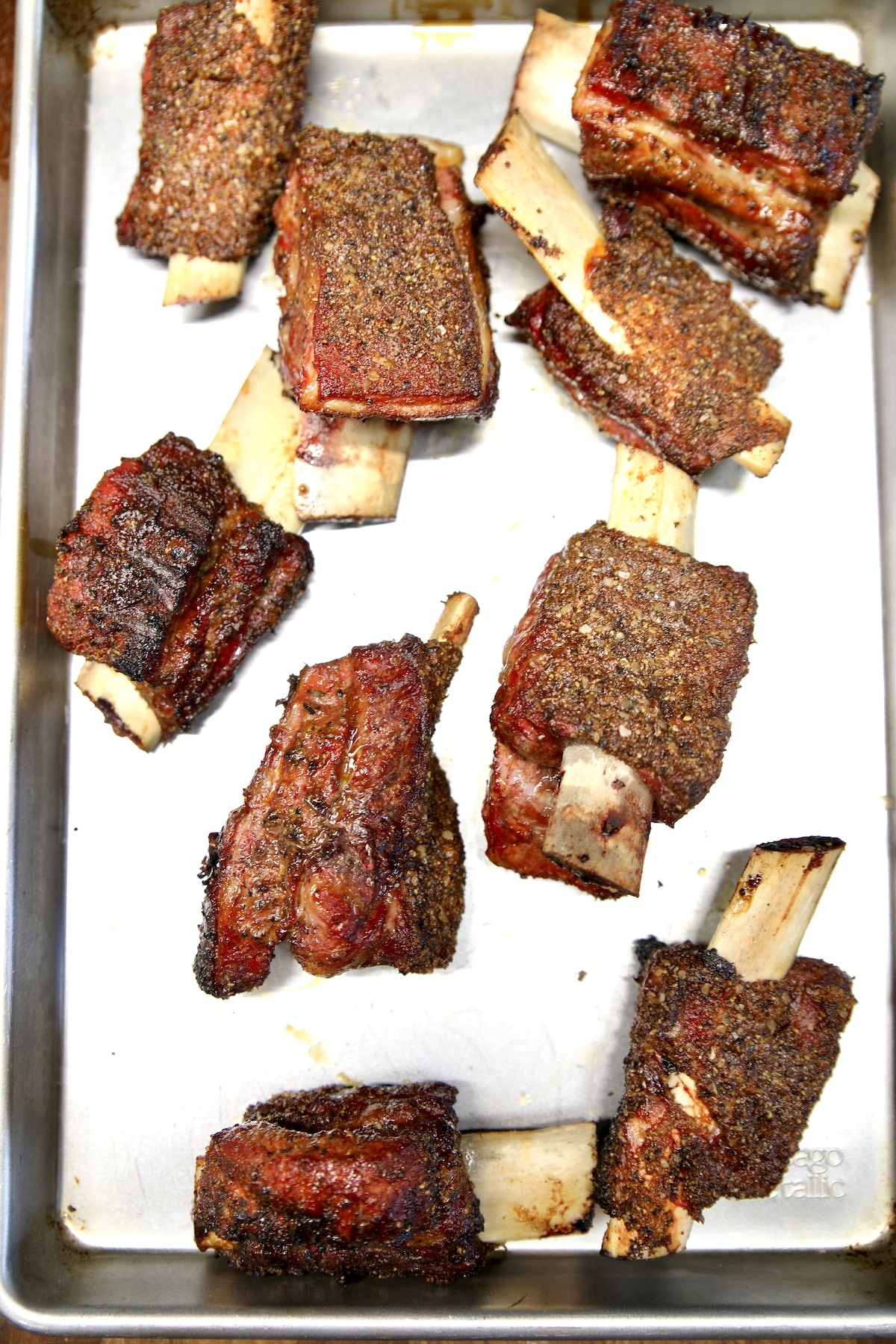 Grilled beef ribs resting on a sheet pan.