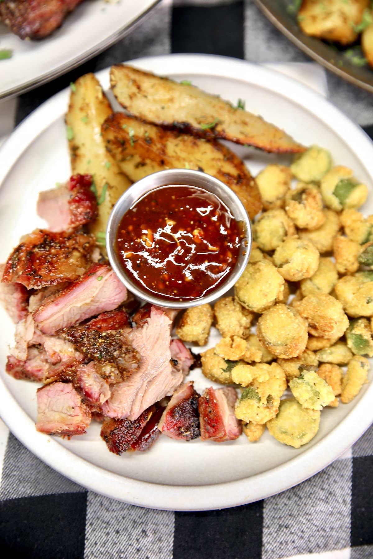 Sliced beef ribs on a plate with fried okra, potatoes and bbq sauce.