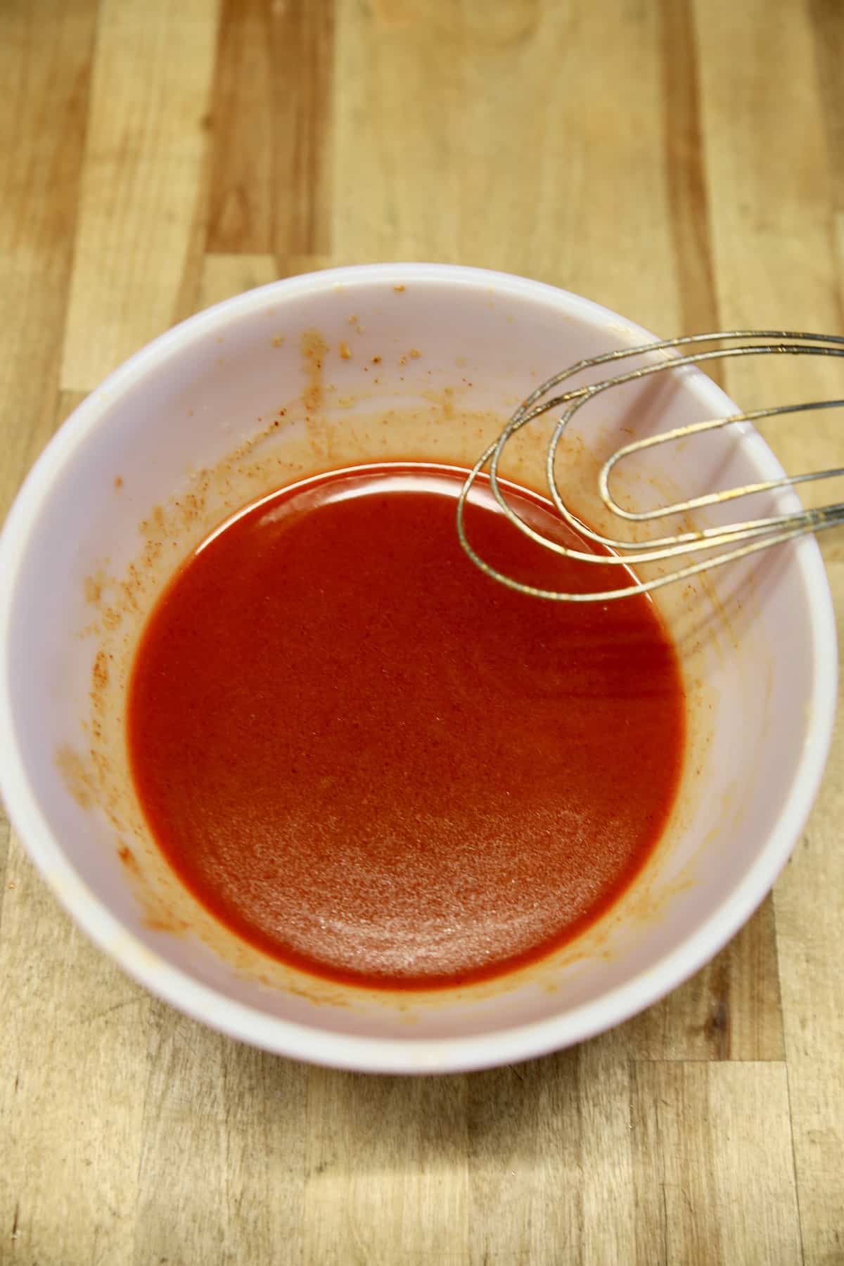 Buffalo sauce in a bowl with whisk on side of bowl.
