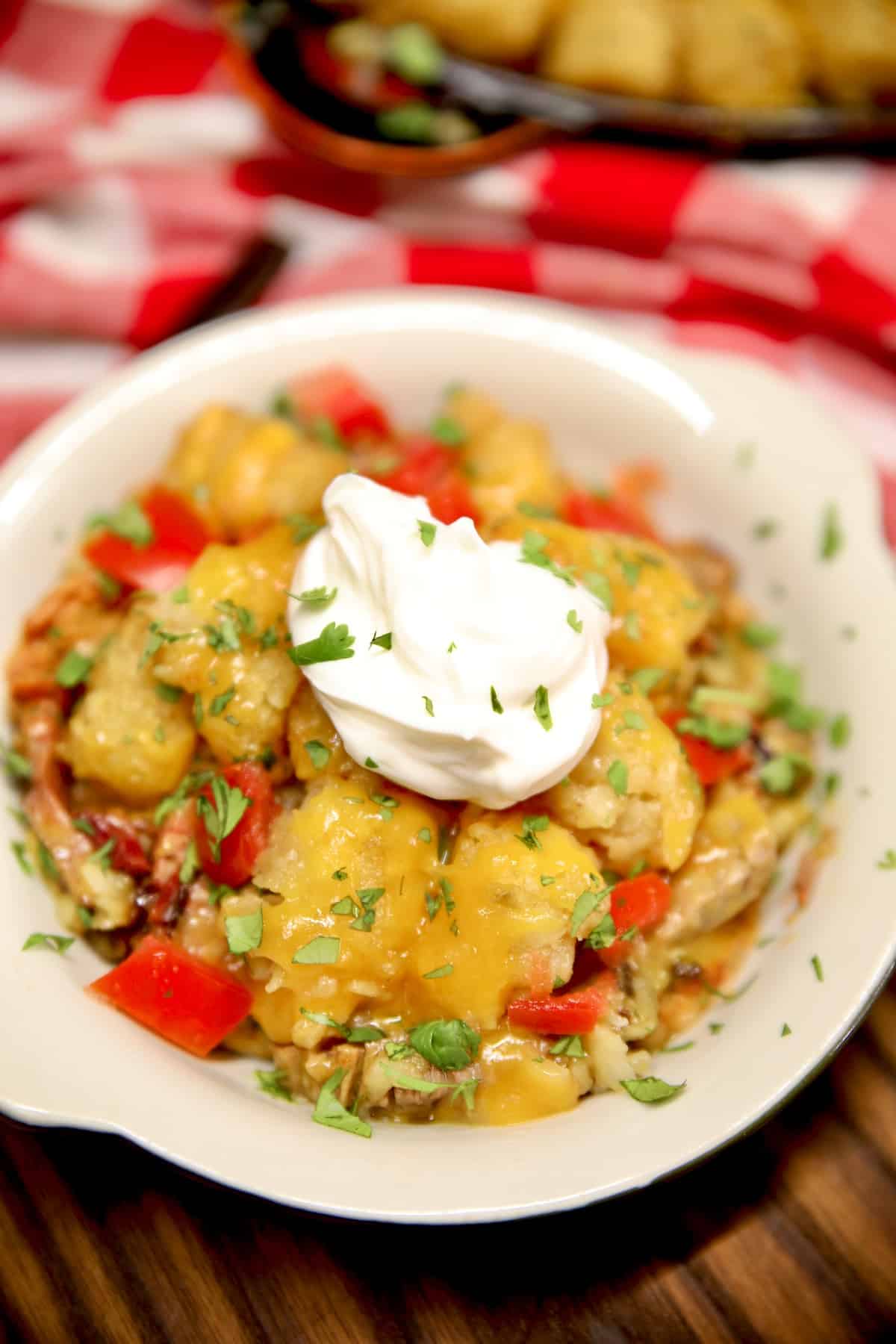 Cowboy Casserole in a bowl with sour cream and tomatoes.