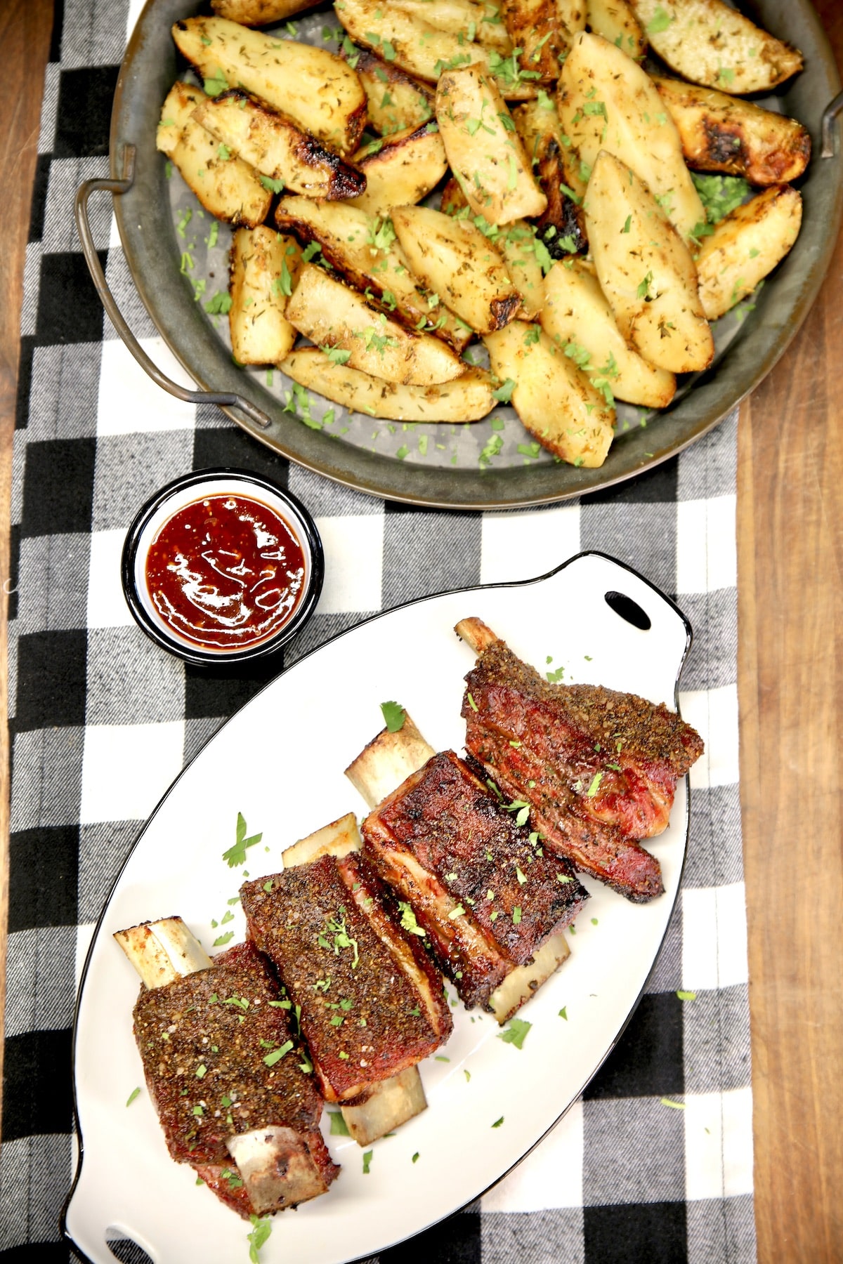 Beef short ribs on a platter with platter of potatoes, bbq sauce.