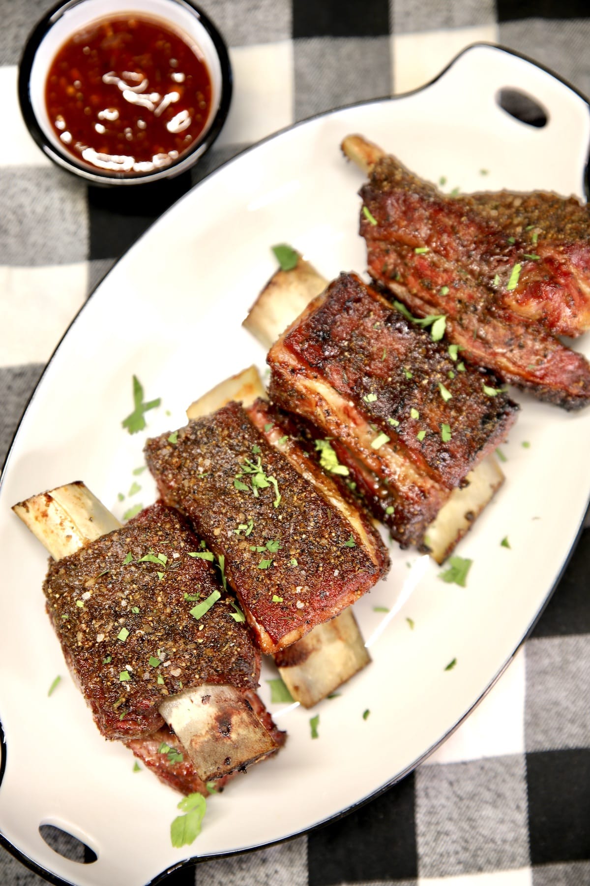 Beef ribs on a platter with bowl of bbq sauce.