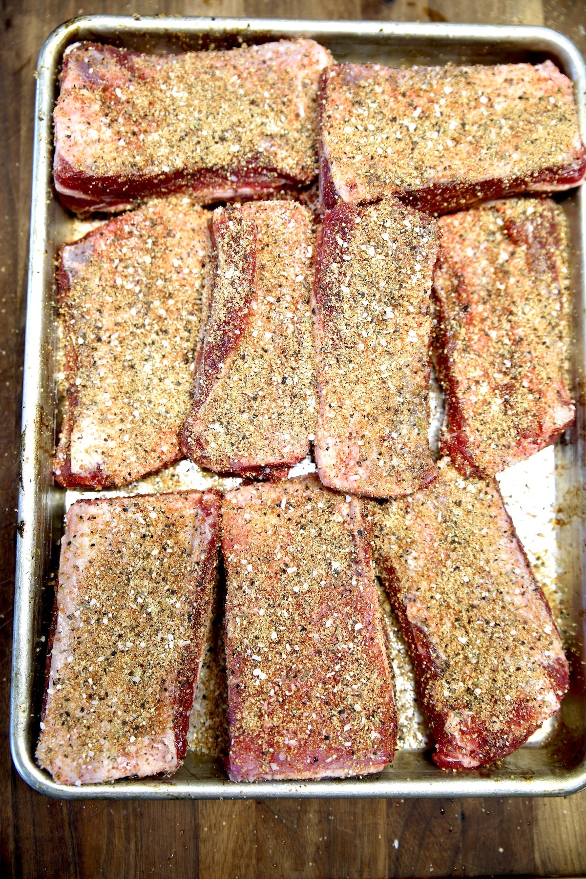 Dry rub seasoned beef ribs on a sheet pan.