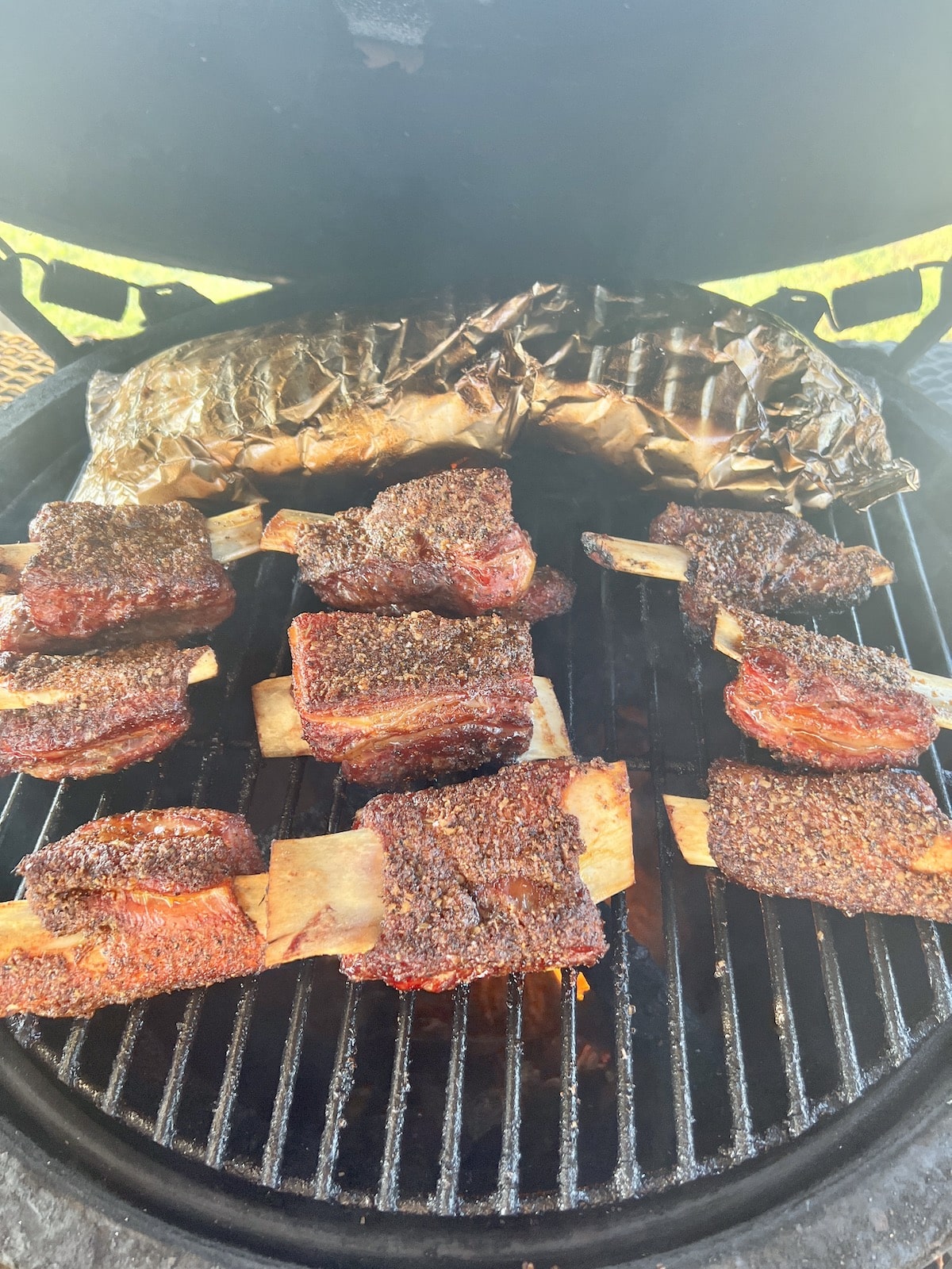 Beef ribs on a grill with a foil packet of potatoes.