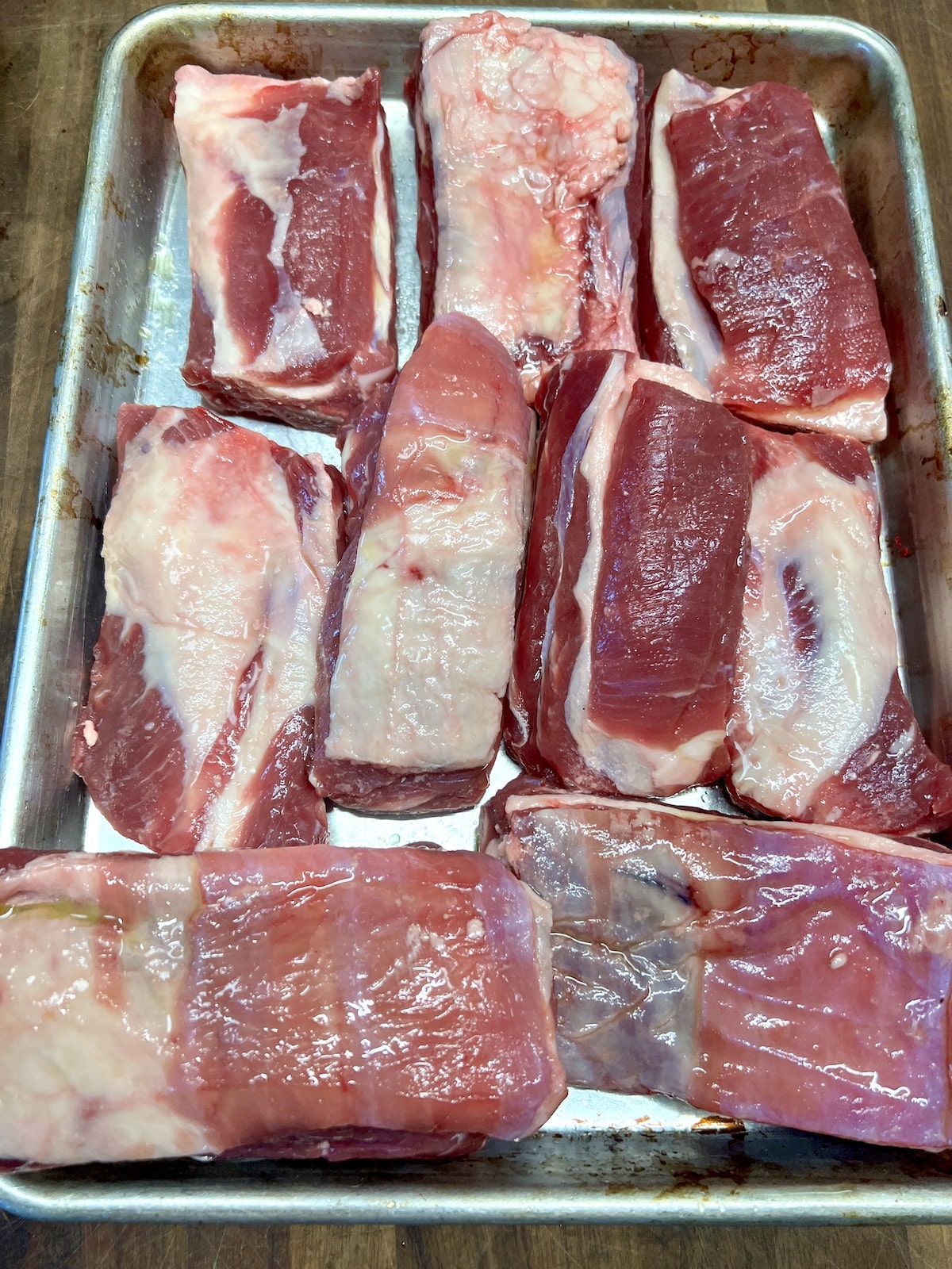 Bone-in beef short ribs, raw, on a pan.