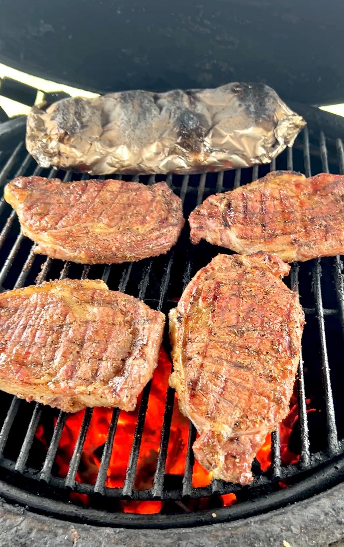 Grilling ribeye steaks with foil packet of potatoes.