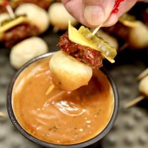 Mini cheeseburger appetizer on a toothpick, dipping into sauce.