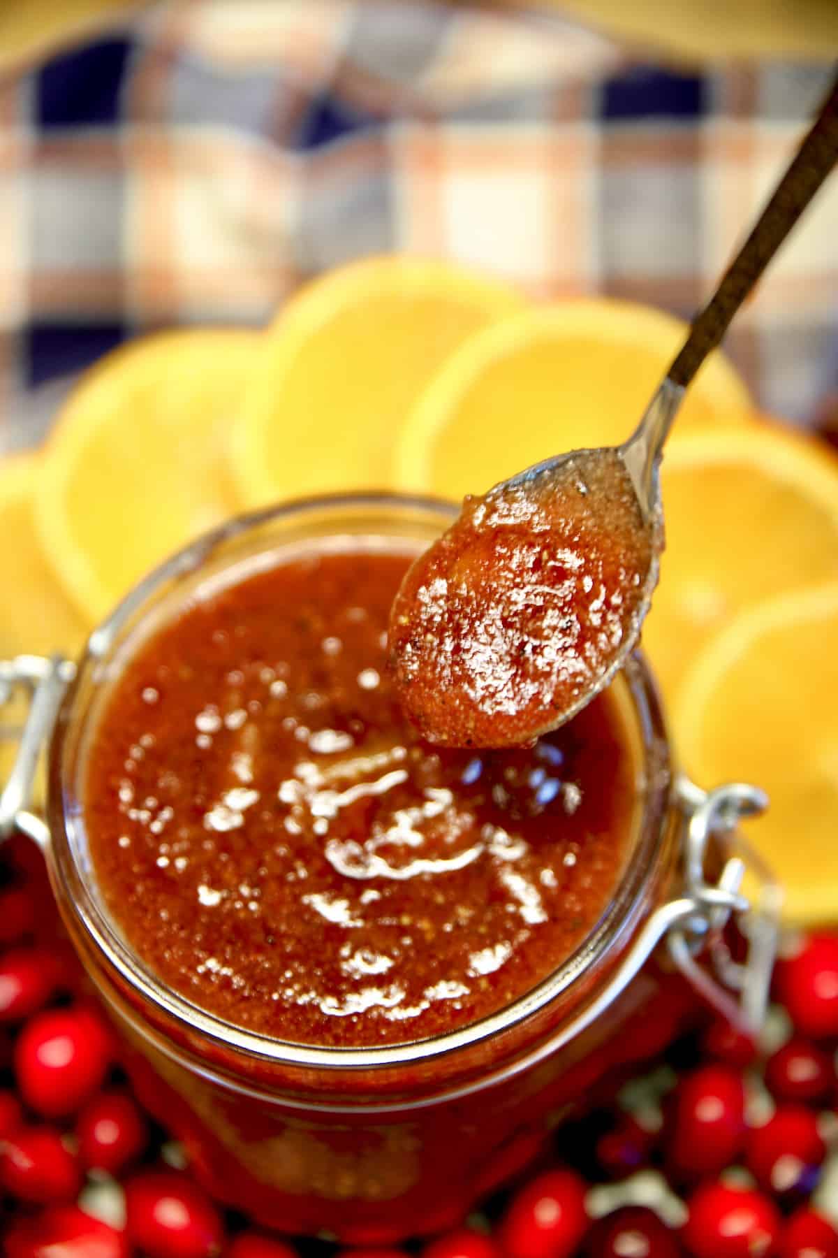 Spoon dipping orange cranberry sauce from a jar.